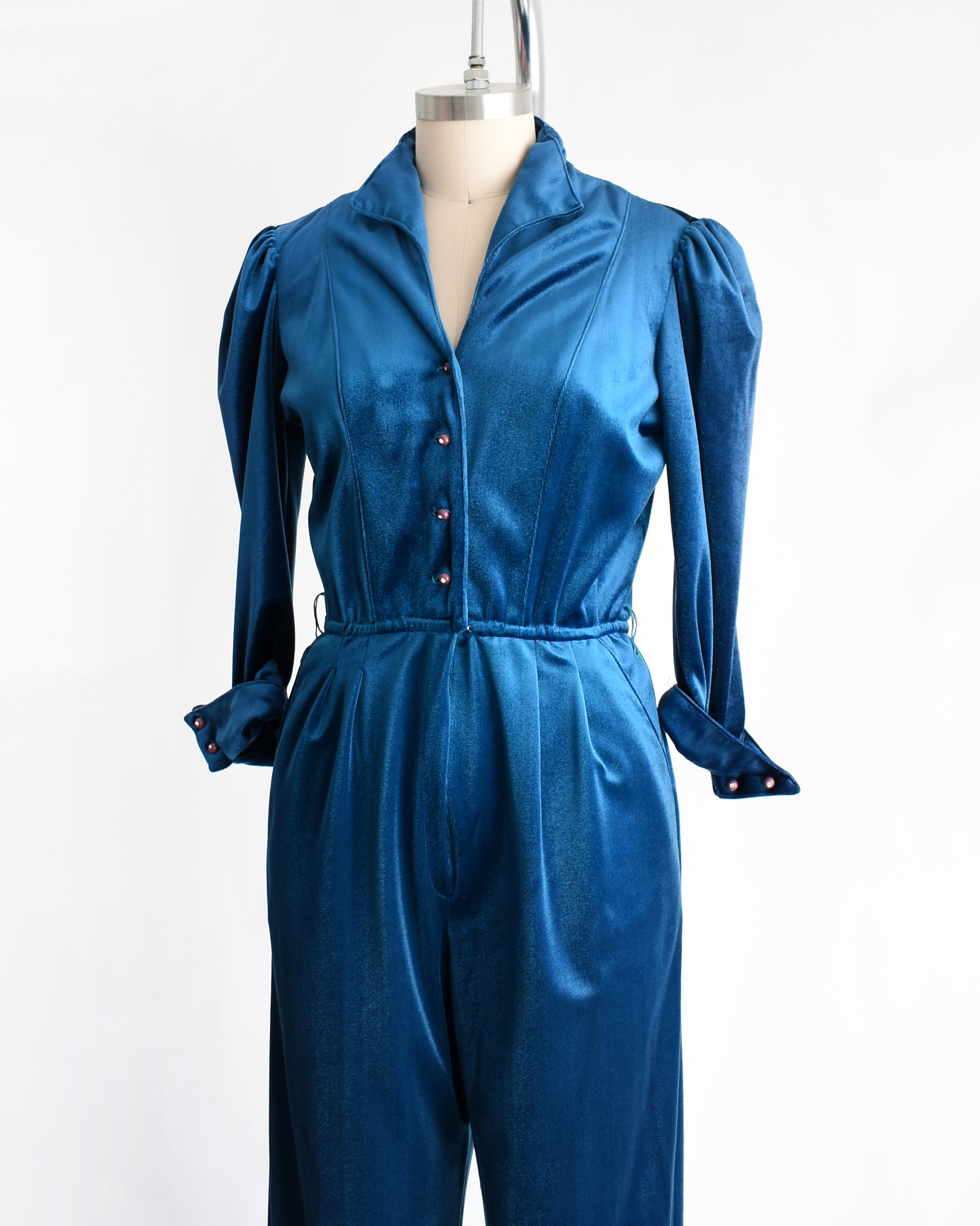 side front view of a vintage 1970s blue velour jumpsuit on a mannequin against a white background