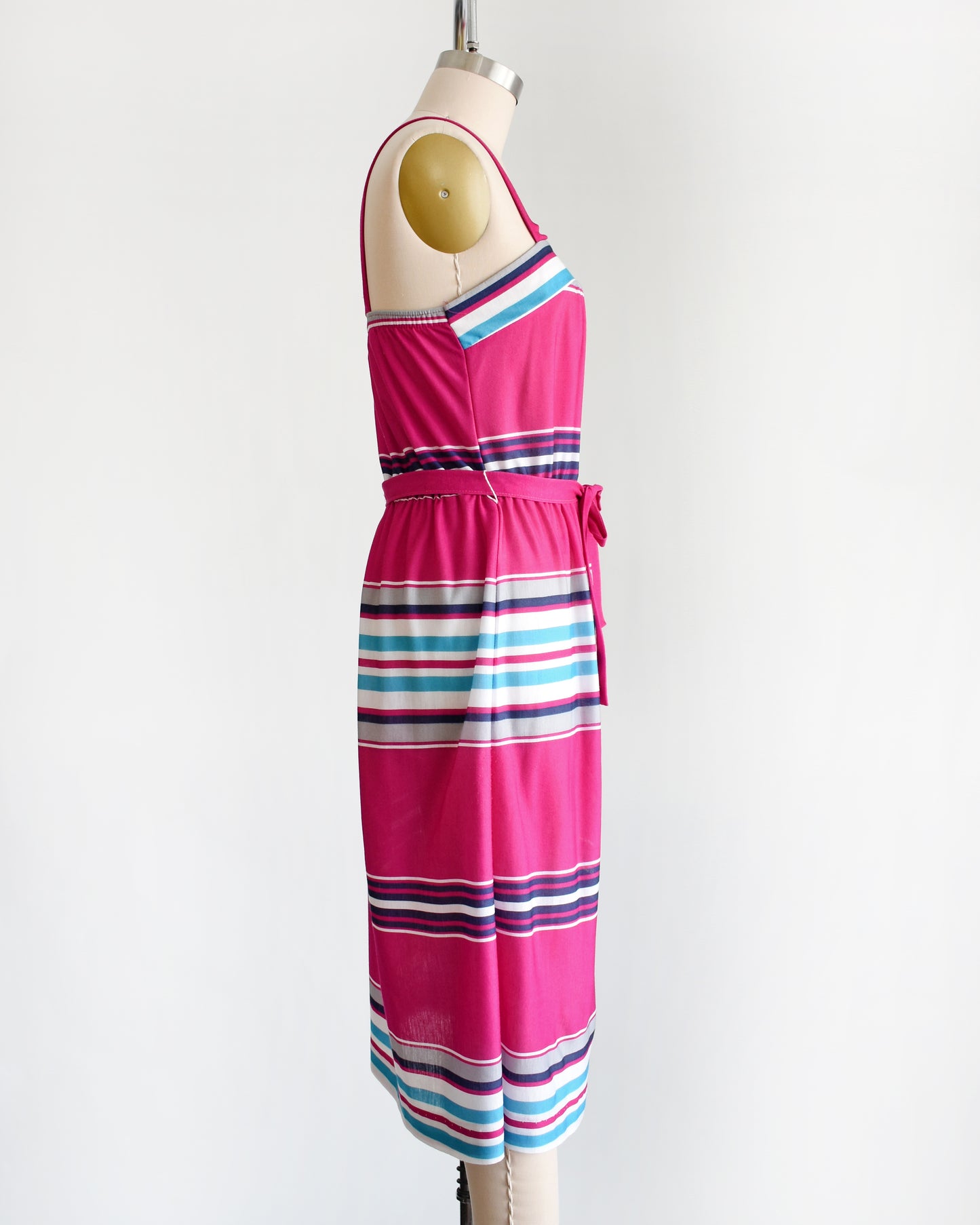 side view of a vintage 1970s/1980s sundress that has horizontal stripes in magenta, light blue, navy blue, gray and white, along with a matching belt.