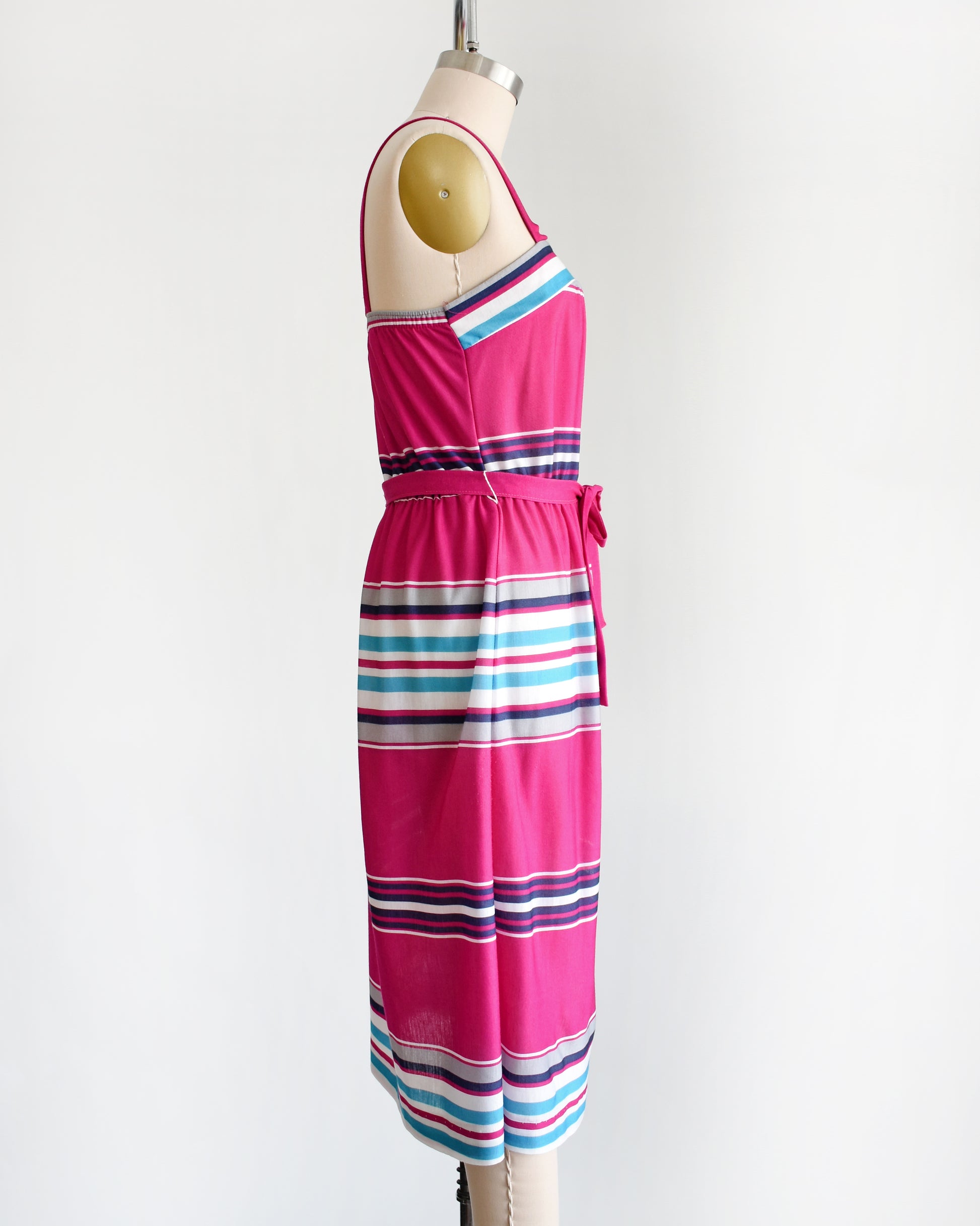 side view of a vintage 1970s/1980s sundress that has horizontal stripes in magenta, light blue, navy blue, gray and white, along with a matching belt.