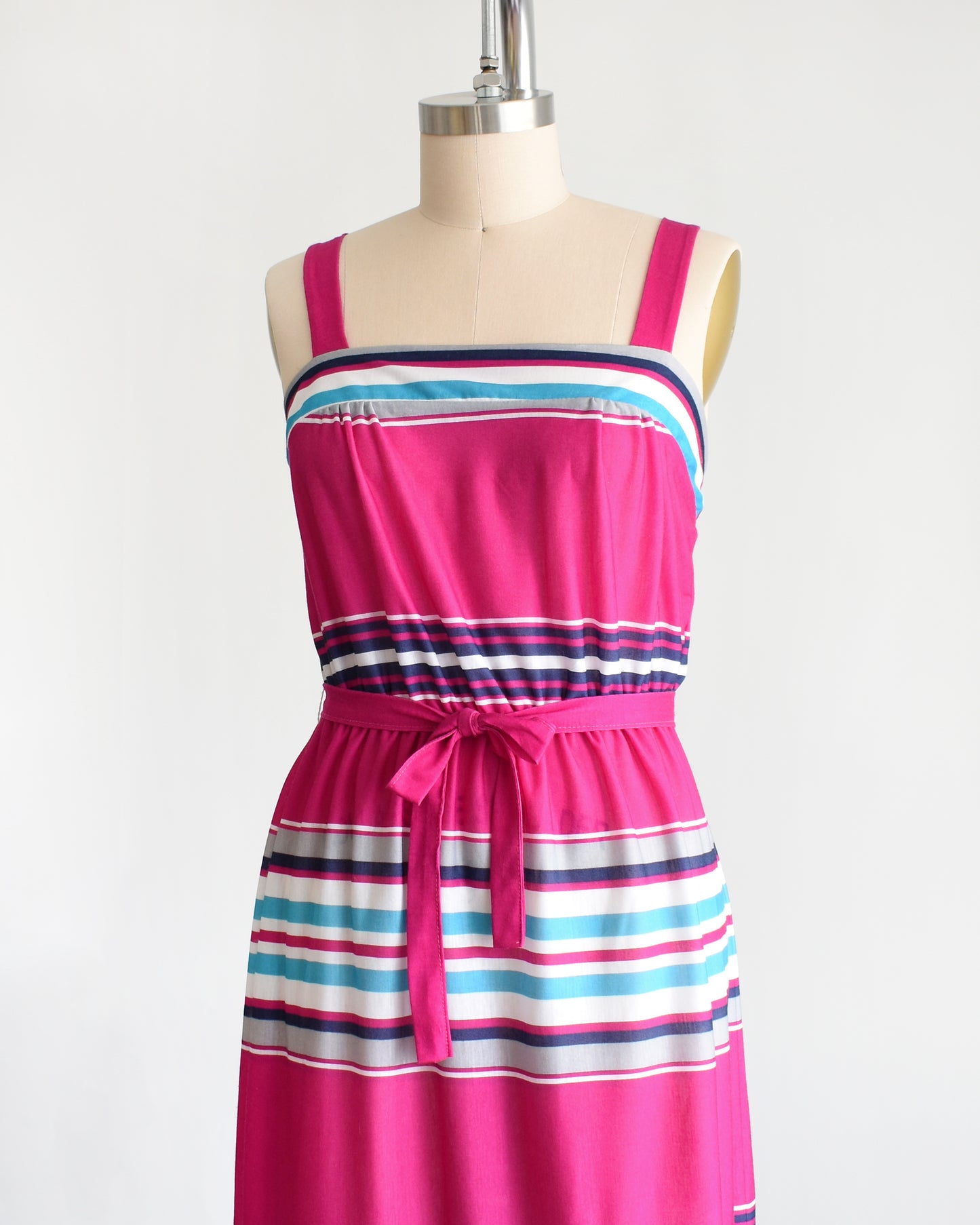 side front view of a vintage 1970s/1980s sundress that has horizontal stripes in magenta, light blue, navy blue, gray and white, along with a matching belt.