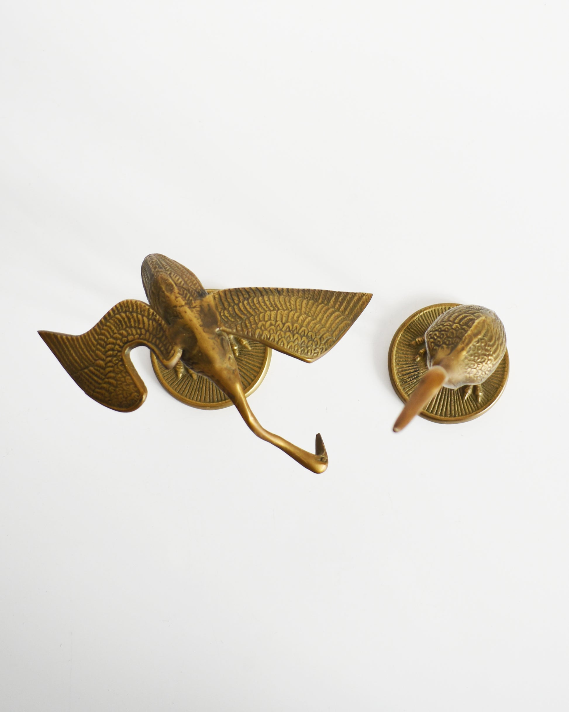 Overhead view of a pair of vintage brass cranes that have ornate carved detail on their wings and body.
