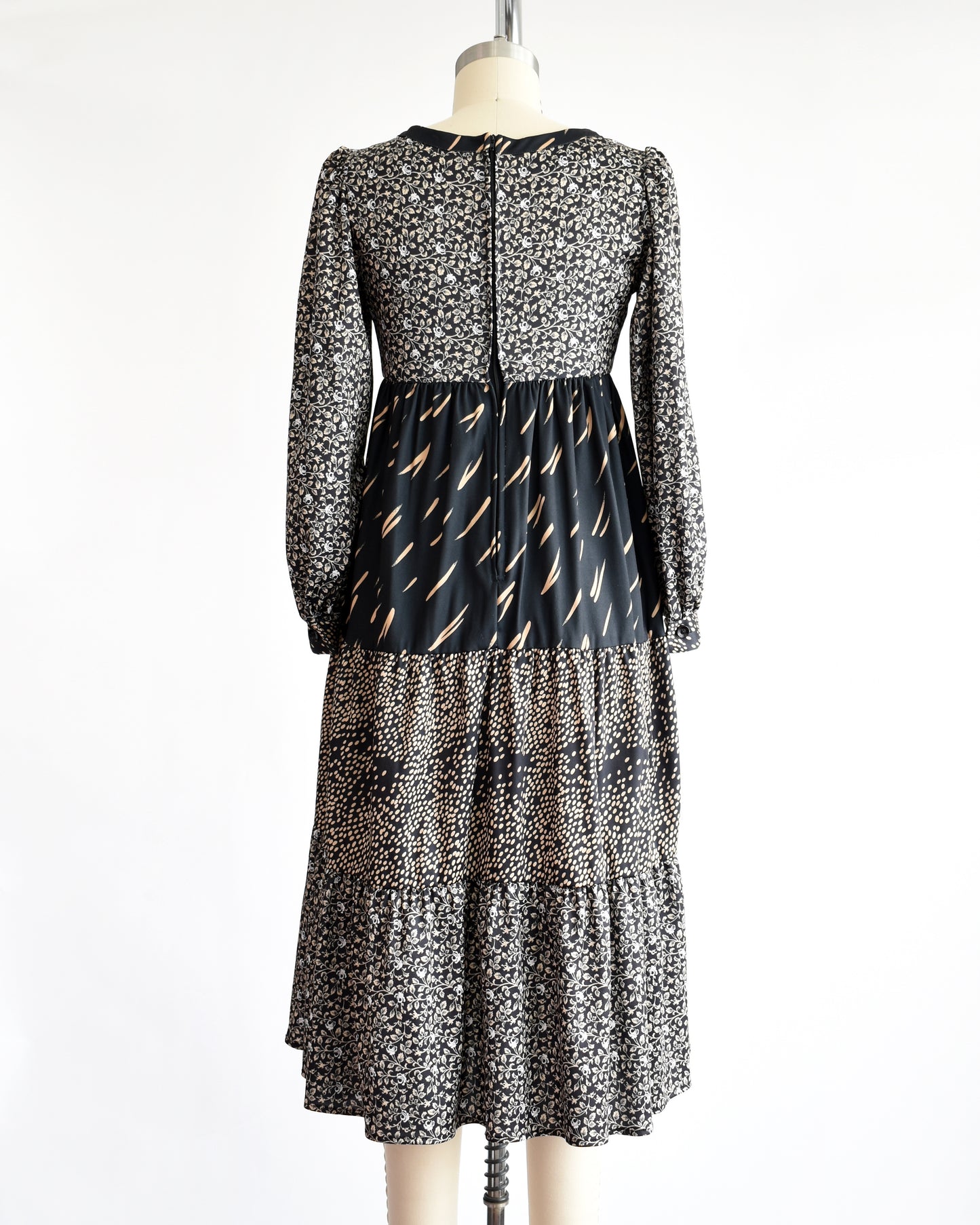 back view of a vintage 1970s black floral dress on a mannequin against a white background