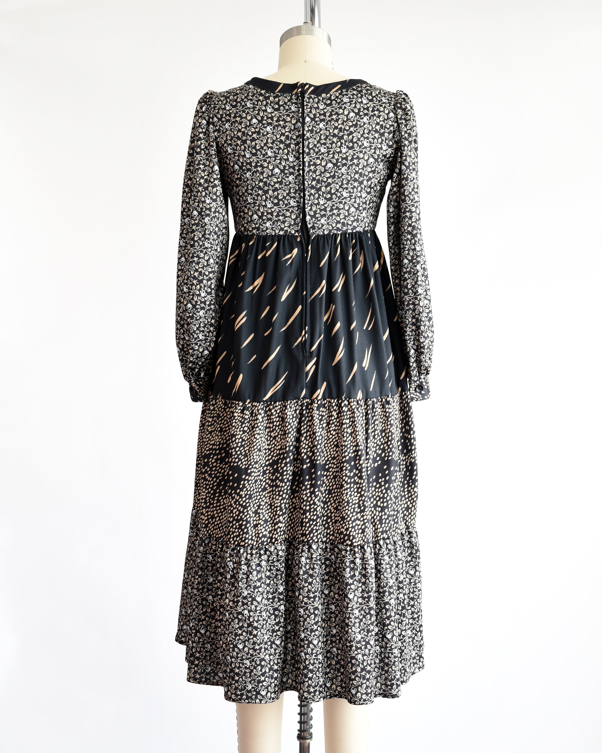 back view of a vintage 1970s black floral dress on a mannequin against a white background