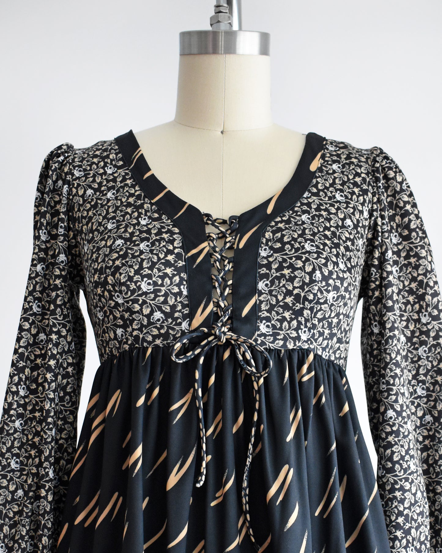 close up of the lace up bodice on a vintage 1970s black floral dress on a mannequin against a white background