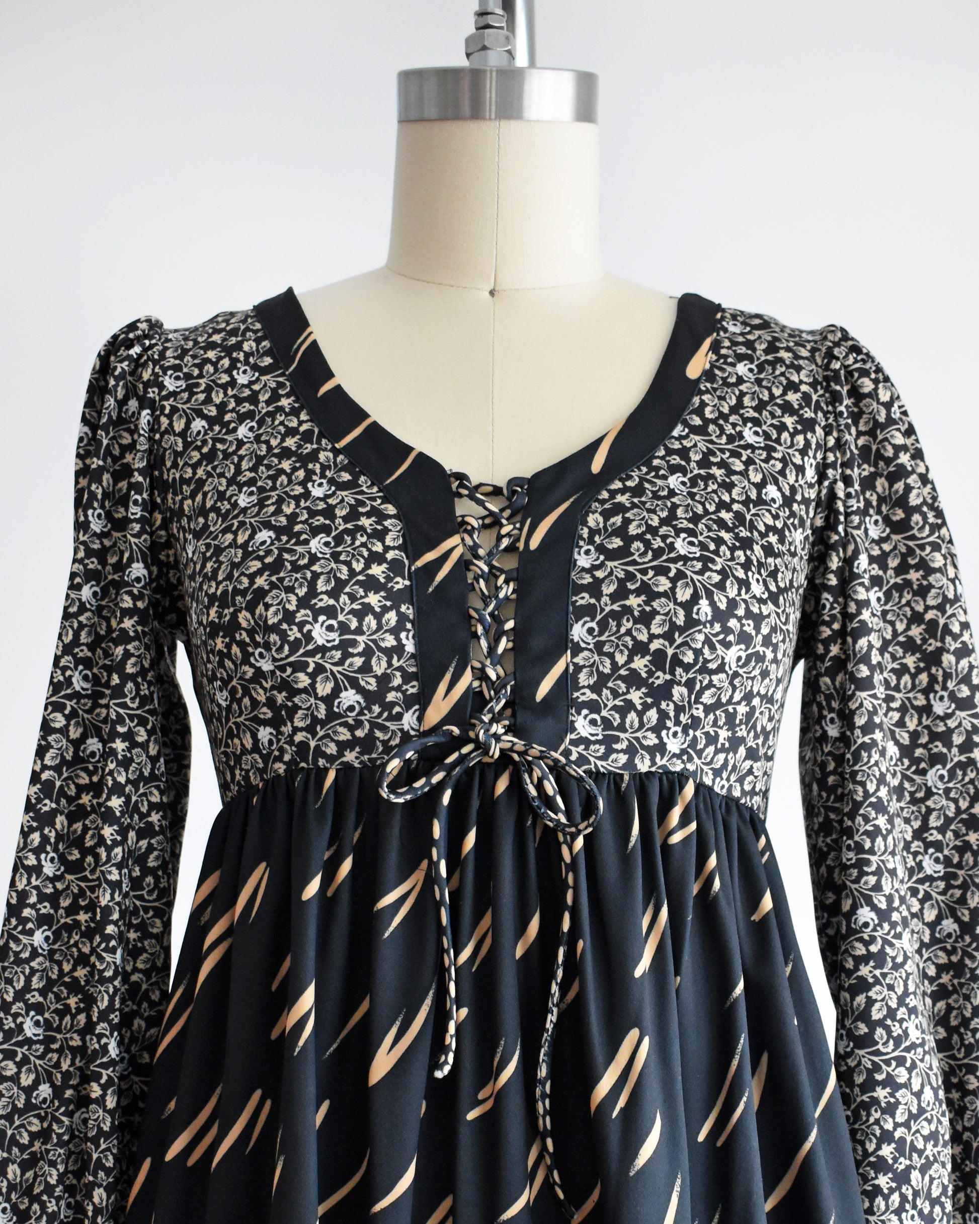 close up of the lace up bodice on a vintage 1970s black floral dress on a mannequin against a white background