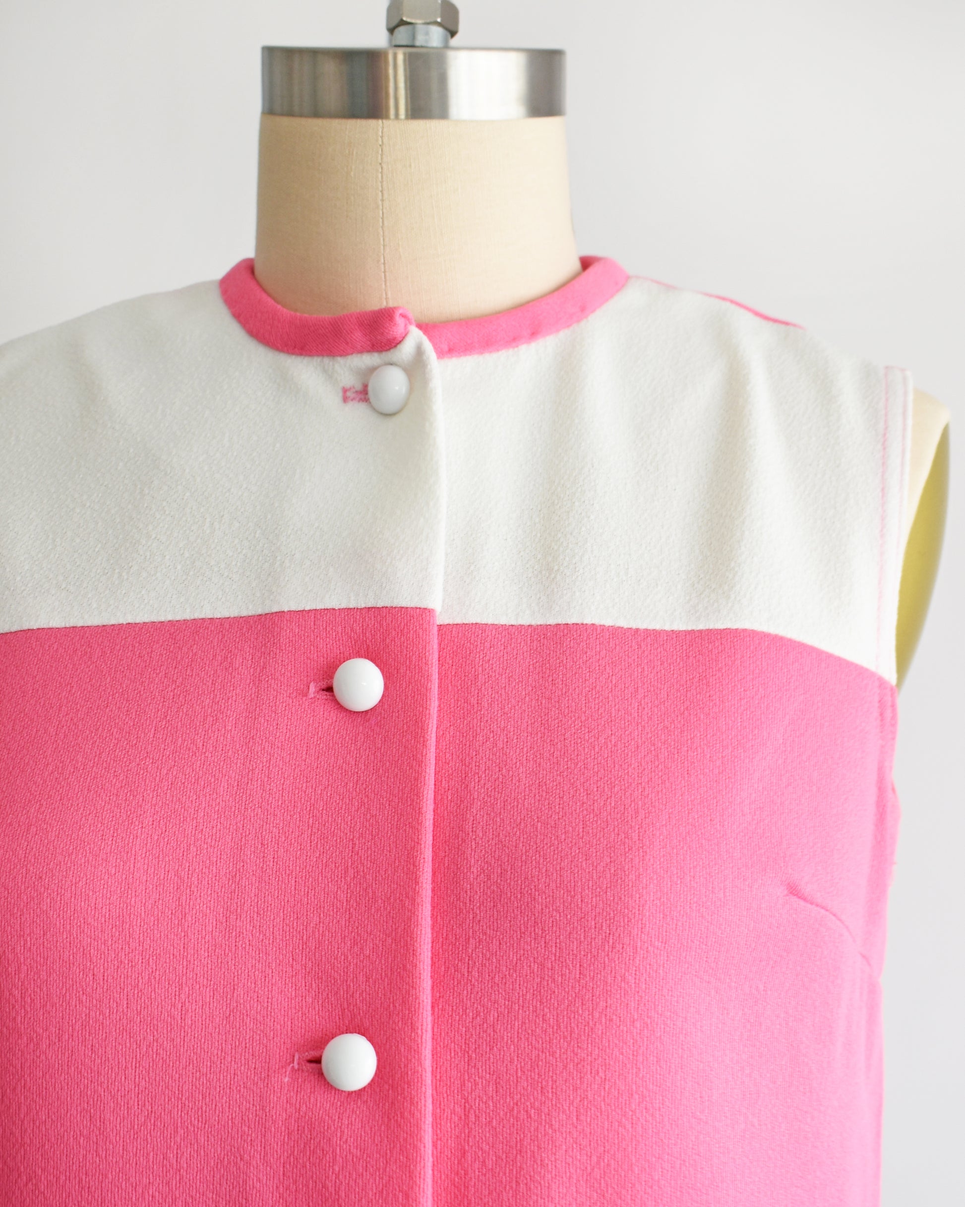 close up of the bodice of a vintage 1960s pink and white mod mini dress that has five white buttons down the front.