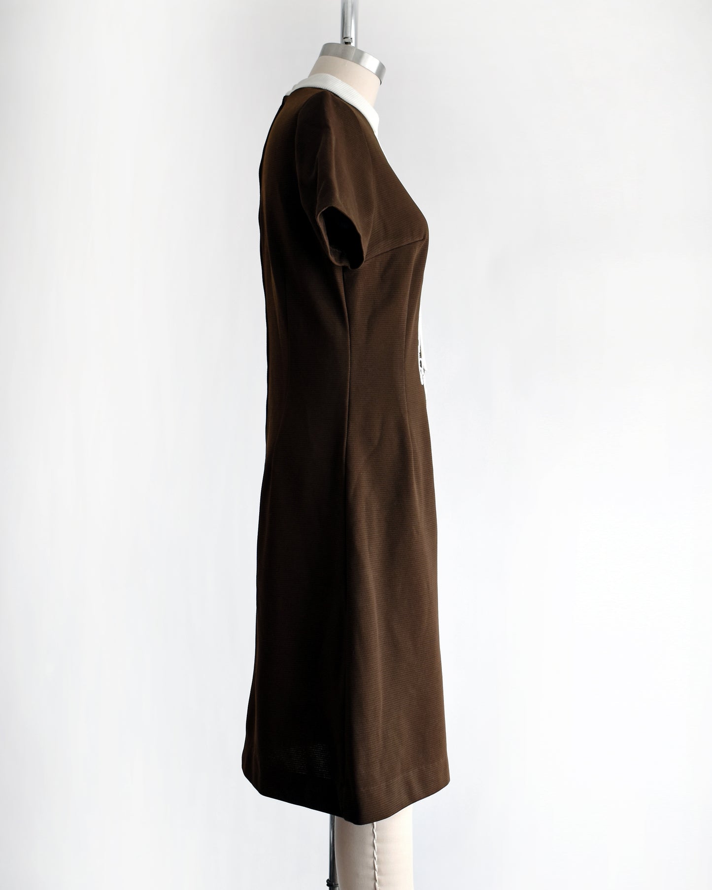 side view of a vintage 1960s brown dress with white embroidery on a mannequin against a white background
