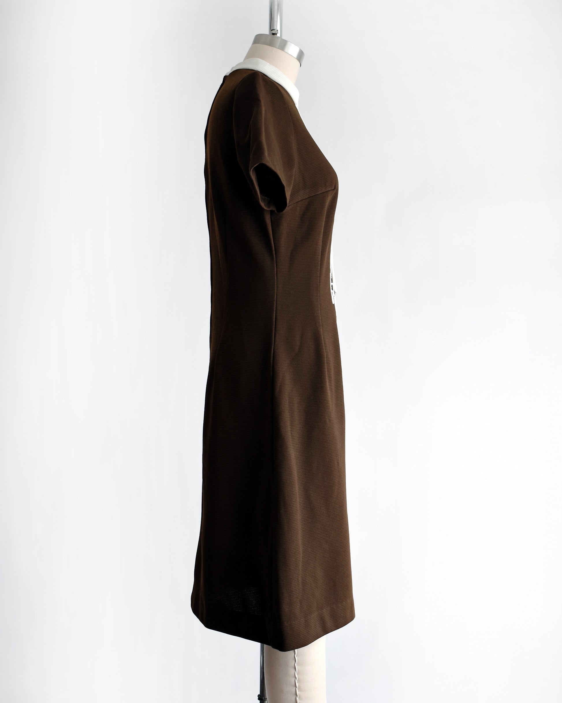 side view of a vintage 1960s brown dress with white embroidery on a mannequin against a white background