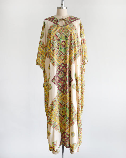 a vintage 1970s caftan thats cream colored with a brown, yellow, and green psychedelic paisley print.