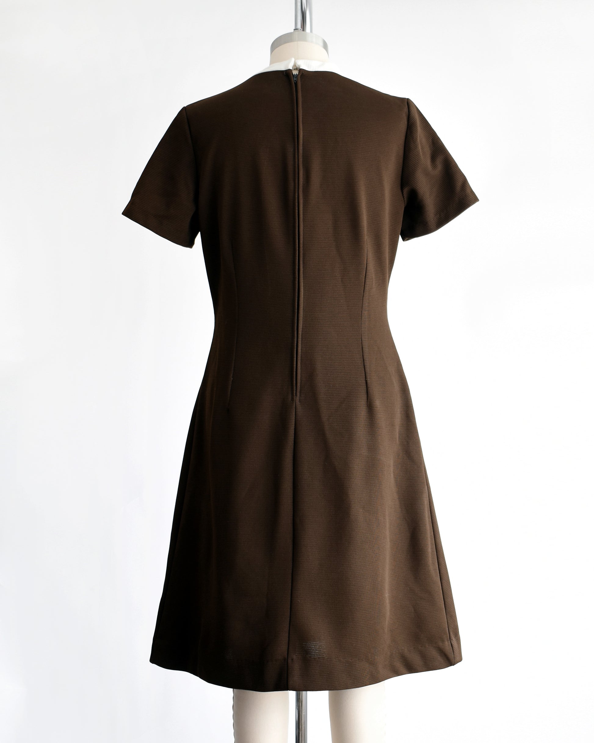 back view of a vintage 1960s brown dress with white embroidery on a mannequin against a white background