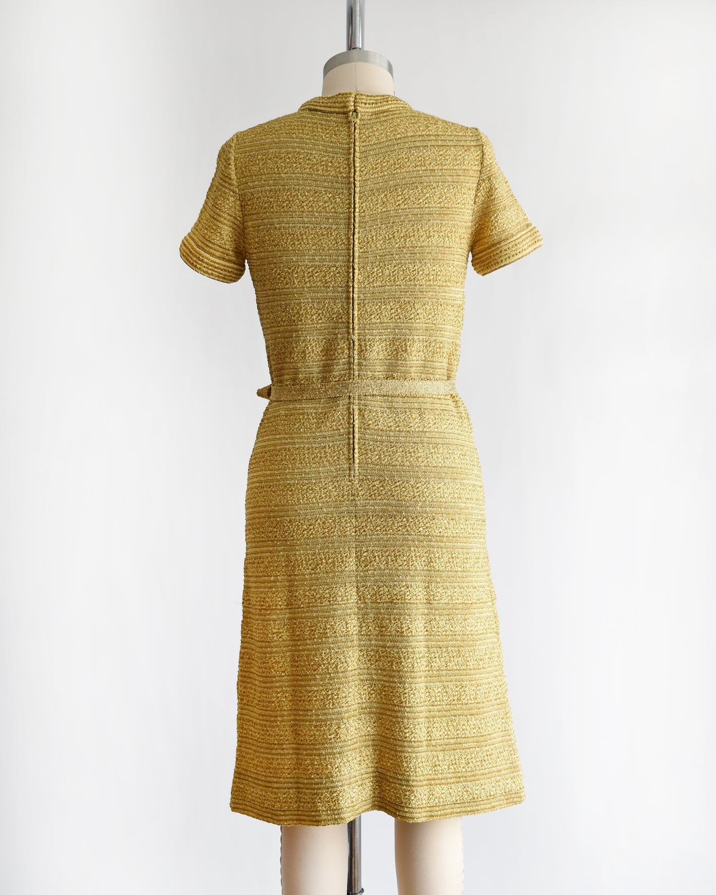 back view of a vintage 1960s gold metallic dress on a mannequin against a white background