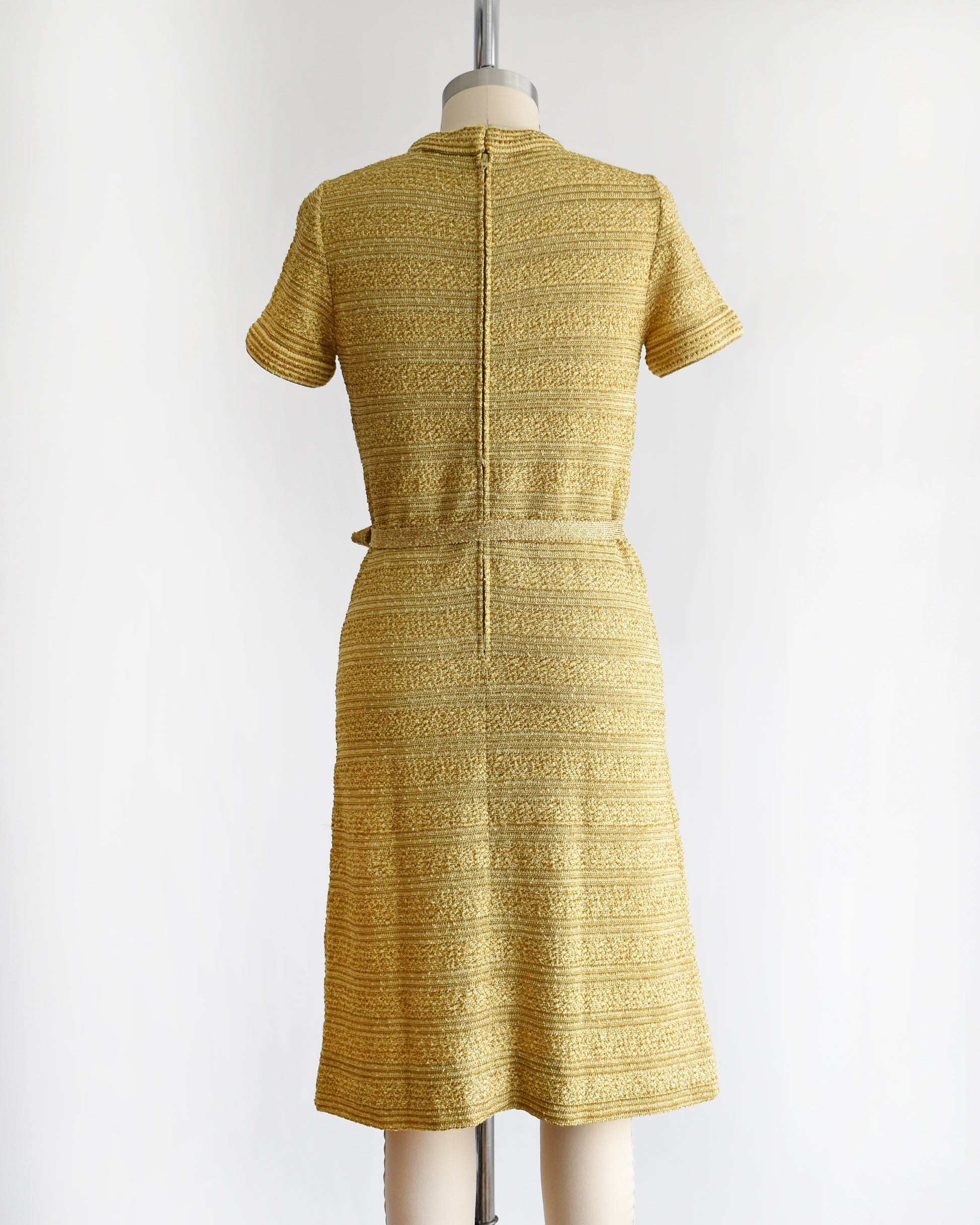 back view of a vintage 1960s gold metallic dress on a mannequin against a white background