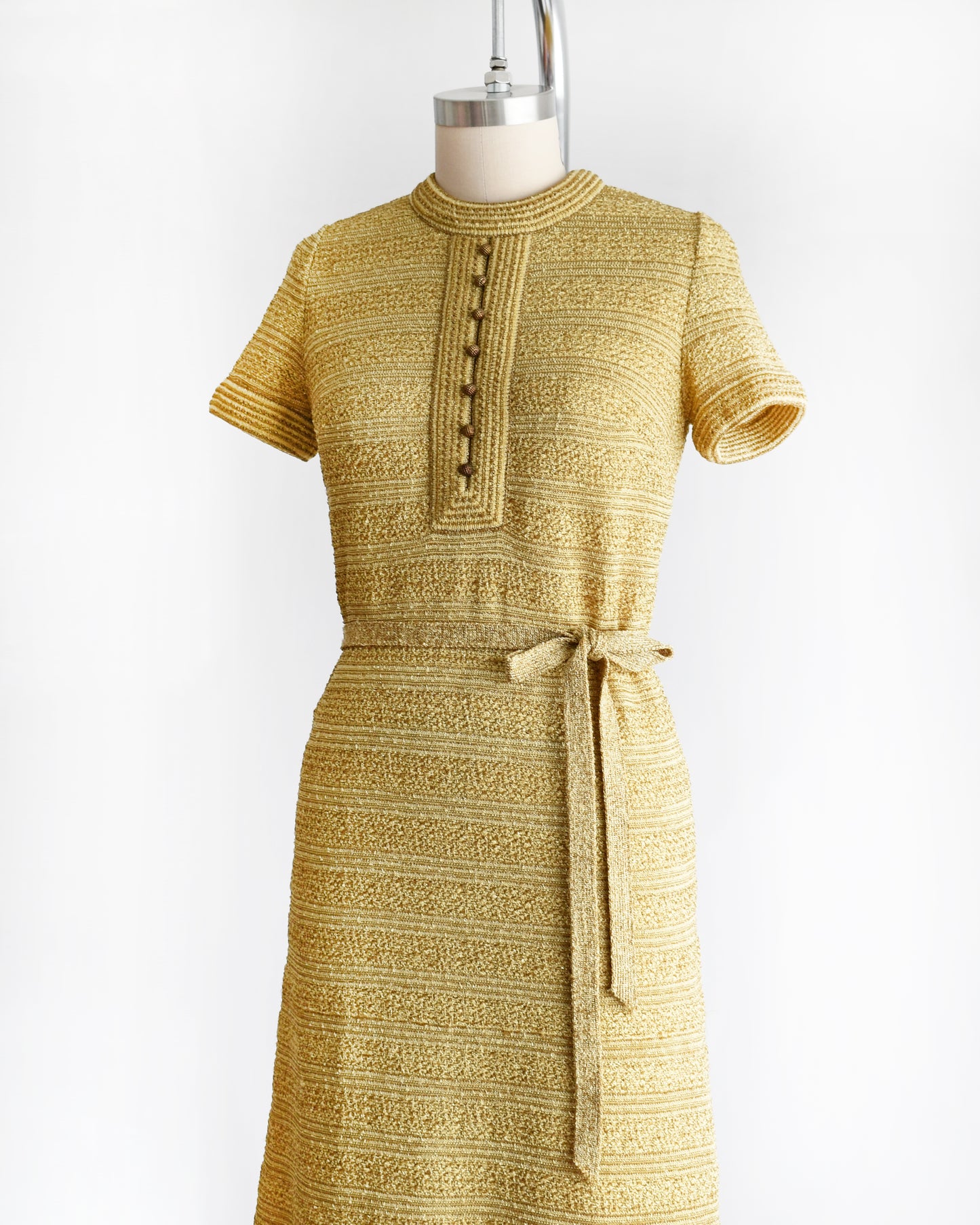 side front view of a vintage 1960s gold metallic dress on a mannequin against a white background