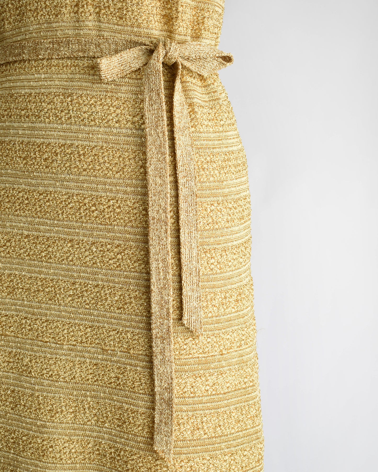 close up of the belt and skirt of a vintage 1960s gold metallic dress on a mannequin against a white background