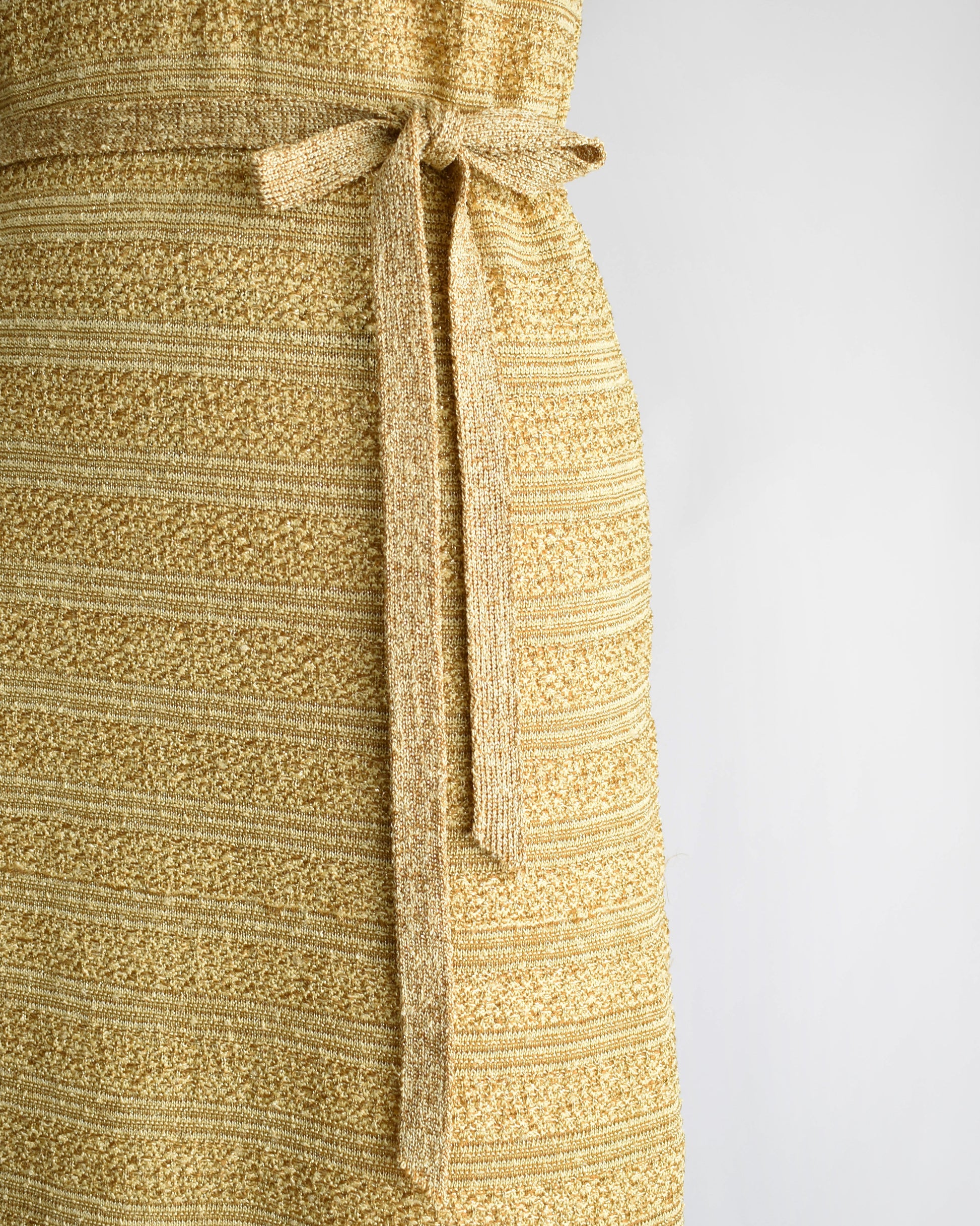close up of the belt and skirt of a vintage 1960s gold metallic dress on a mannequin against a white background