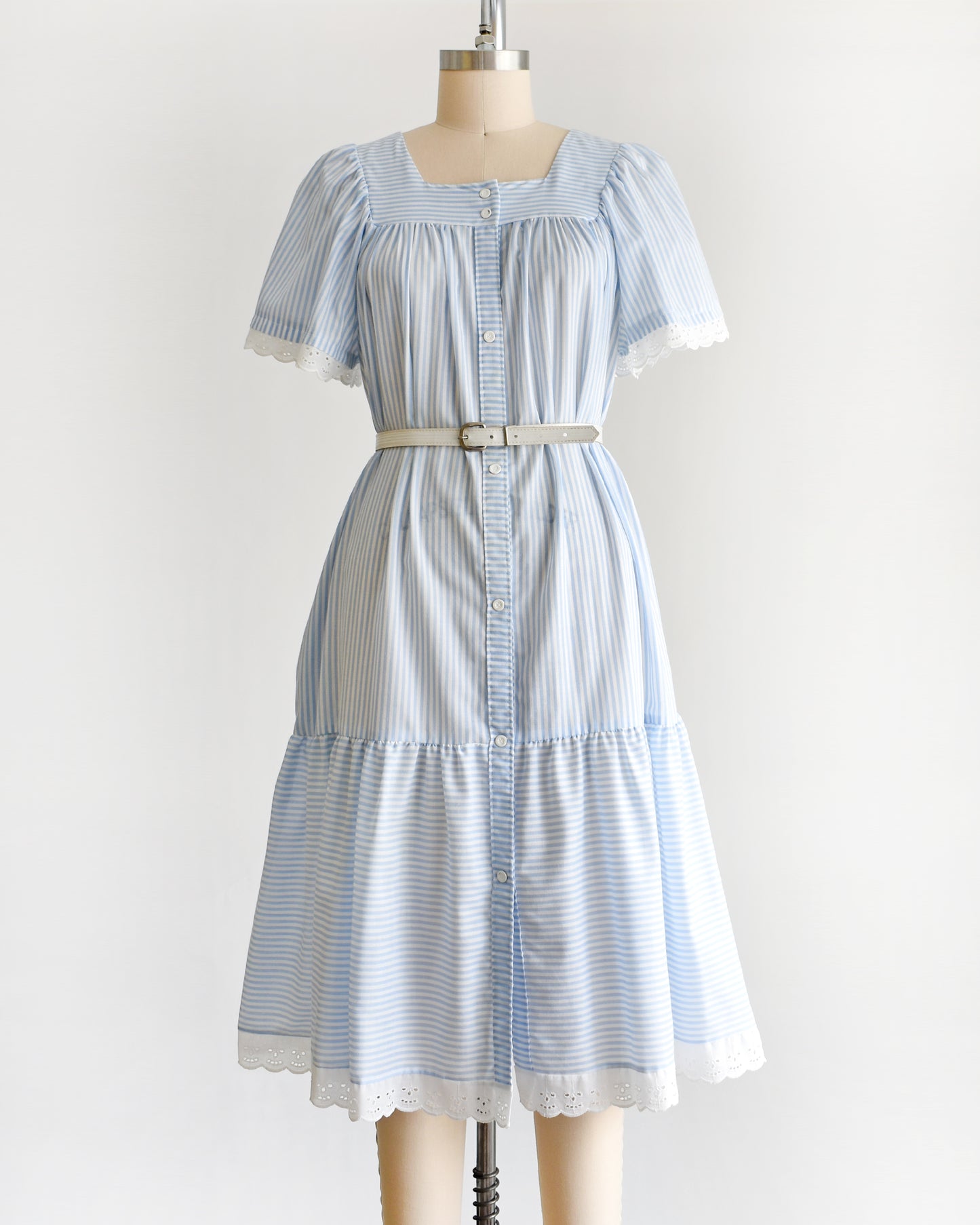 a vintage 1980s blue and white striped dress on a mannequin against a white background. The dress is shown with a belt, which is not included.