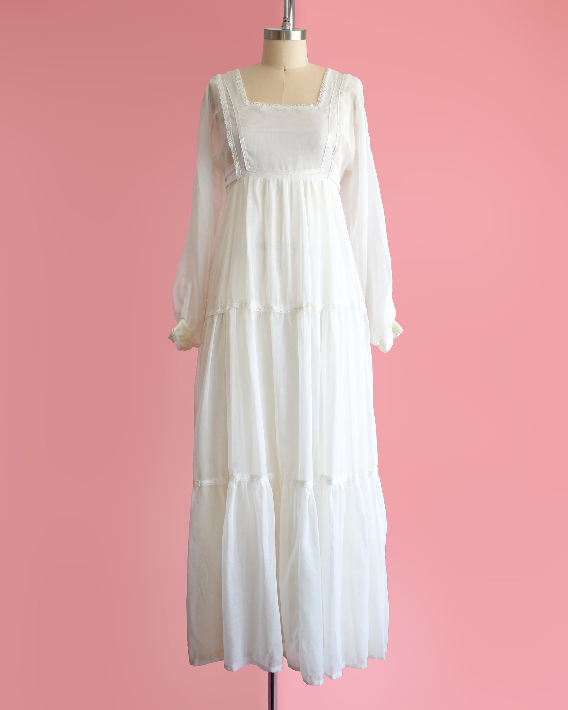 a vintage 1970s white maxi dress on a mannequin against a pink background