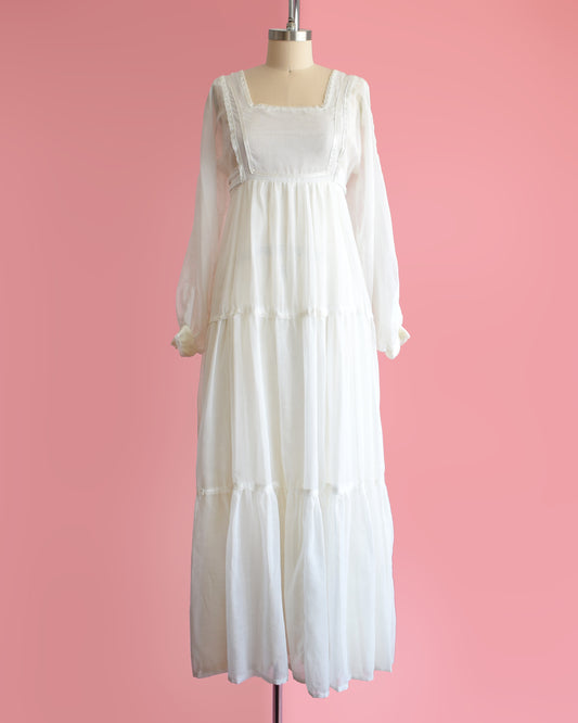 a vintage 1970s white maxi dress on a mannequin against a pink background