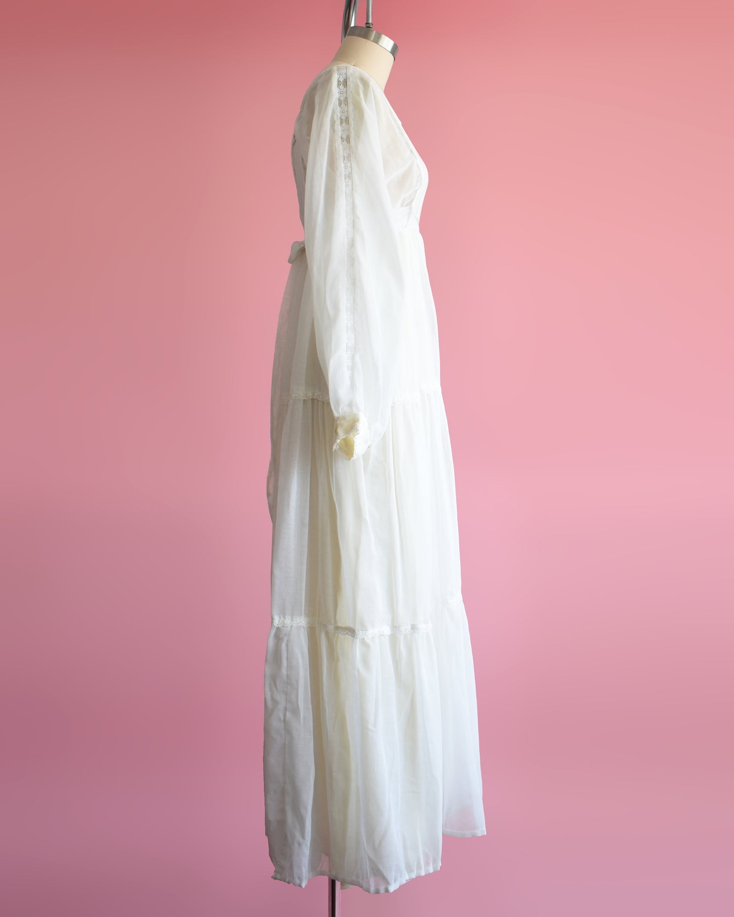 side view of a vintage 1970s white maxi dress on a mannequin against a pink background