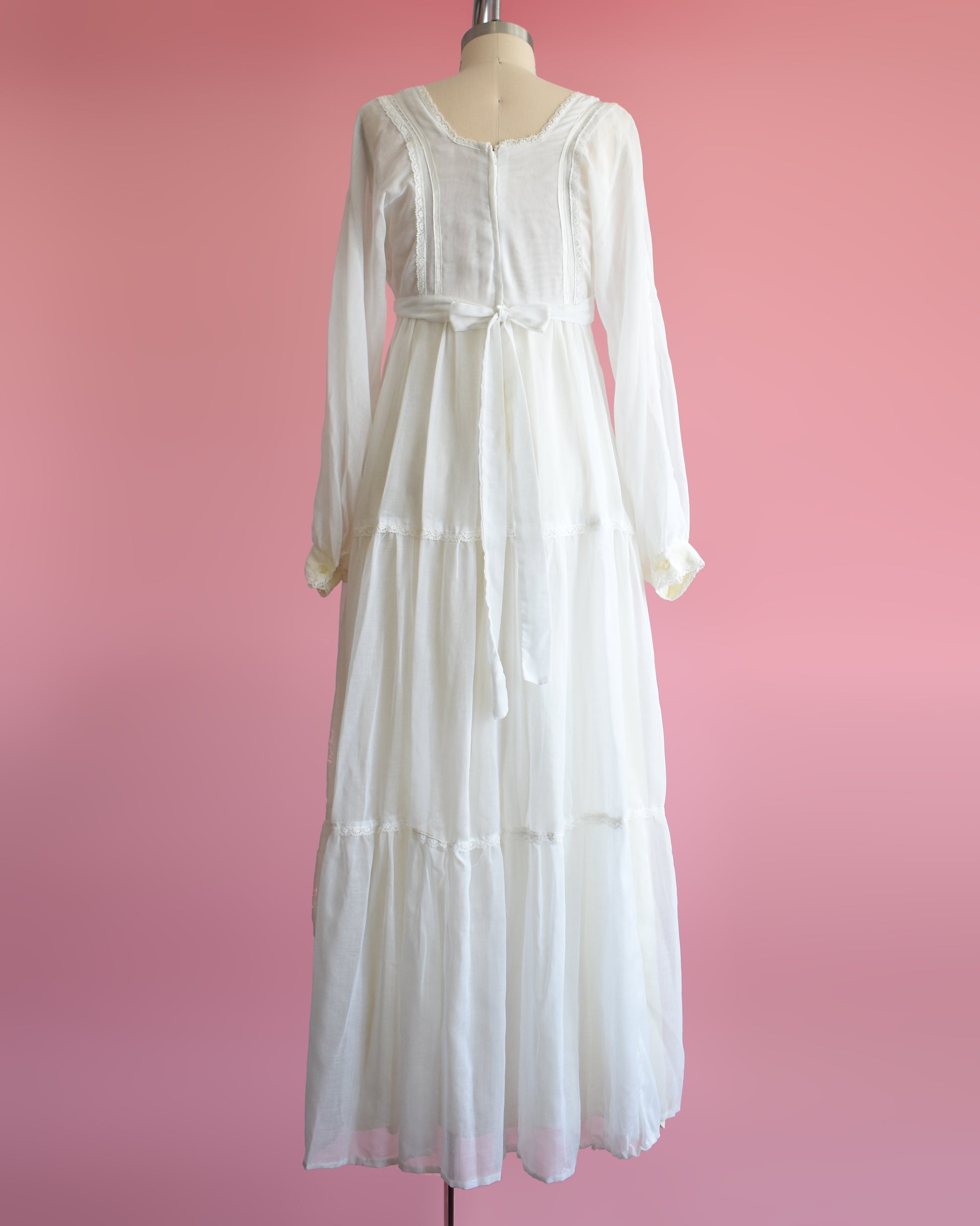 back view of a vintage 1970s white maxi dress on a mannequin against a pink background