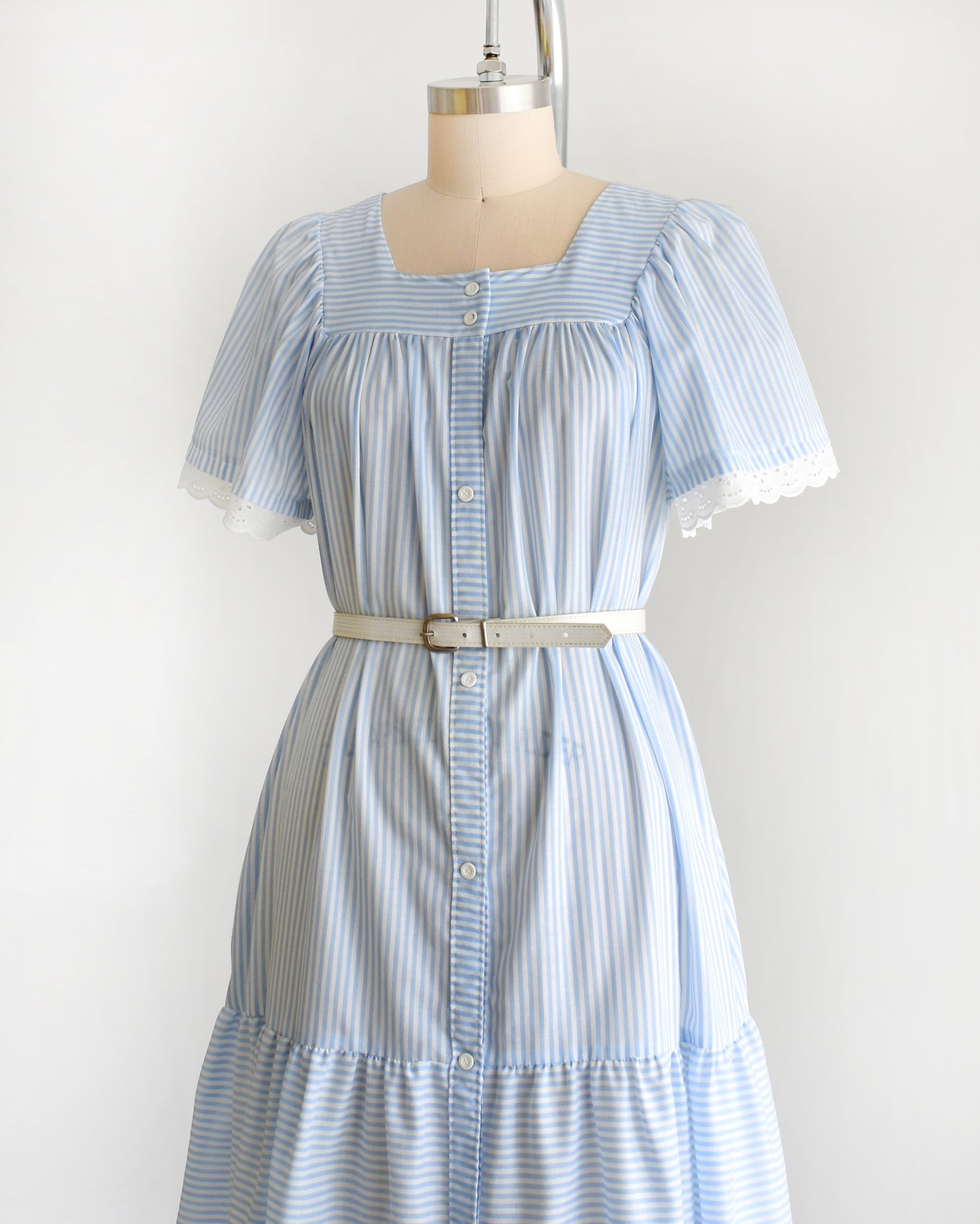 side front view of a vintage 1980s blue and white striped dress on a mannequin against a white background. The dress is shown with a belt, which is not included.