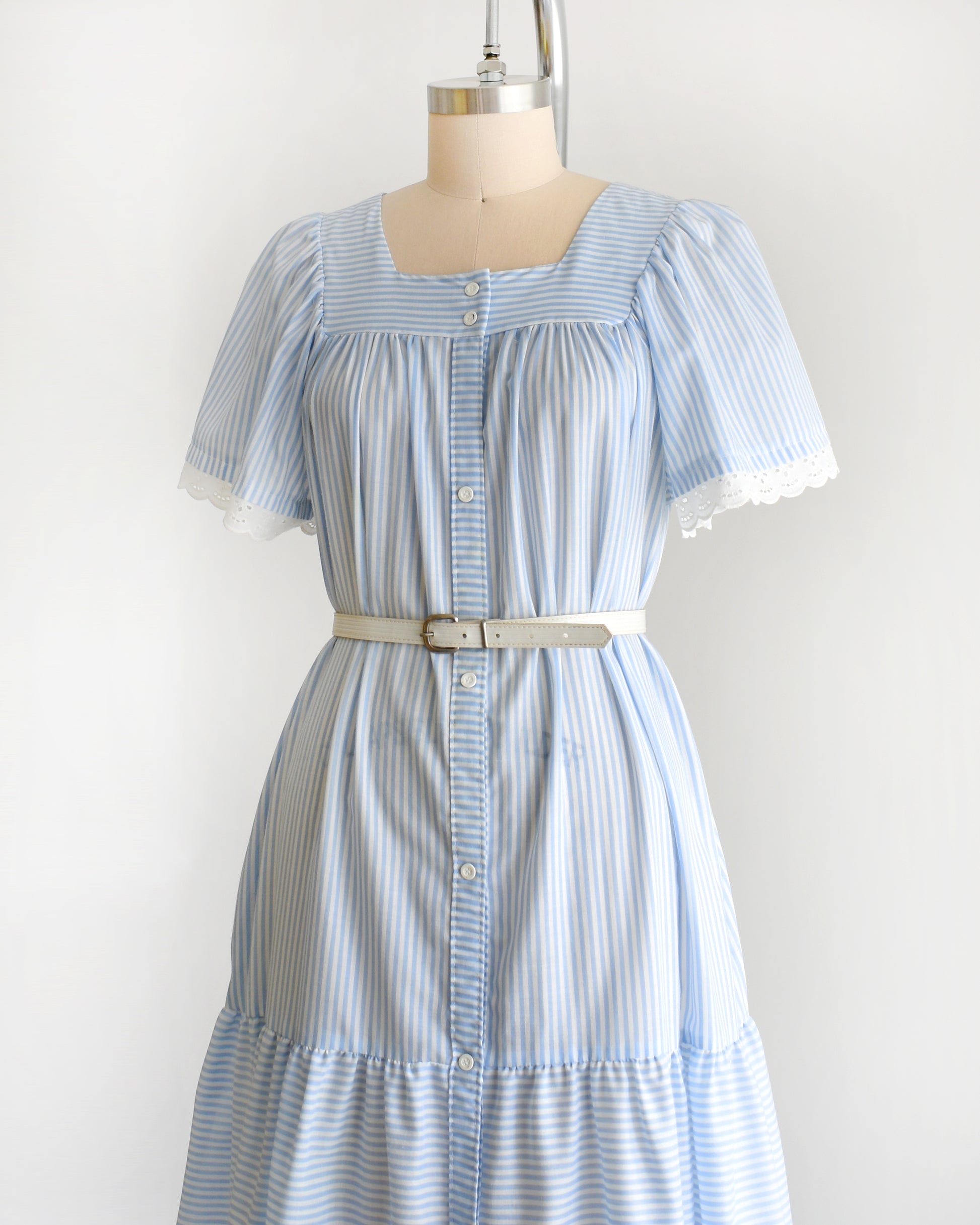 side front view of a vintage 1980s blue and white striped dress on a mannequin against a white background. The dress is shown with a belt, which is not included.