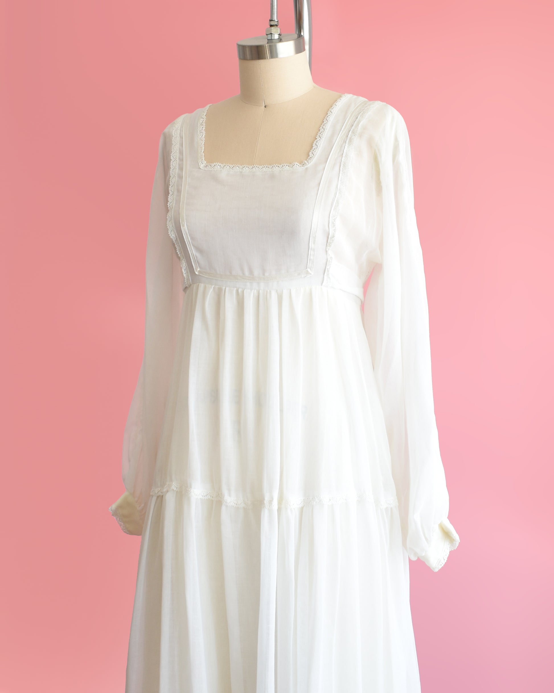 side front view of a vintage 1970s white maxi dress on a mannequin against a pink background