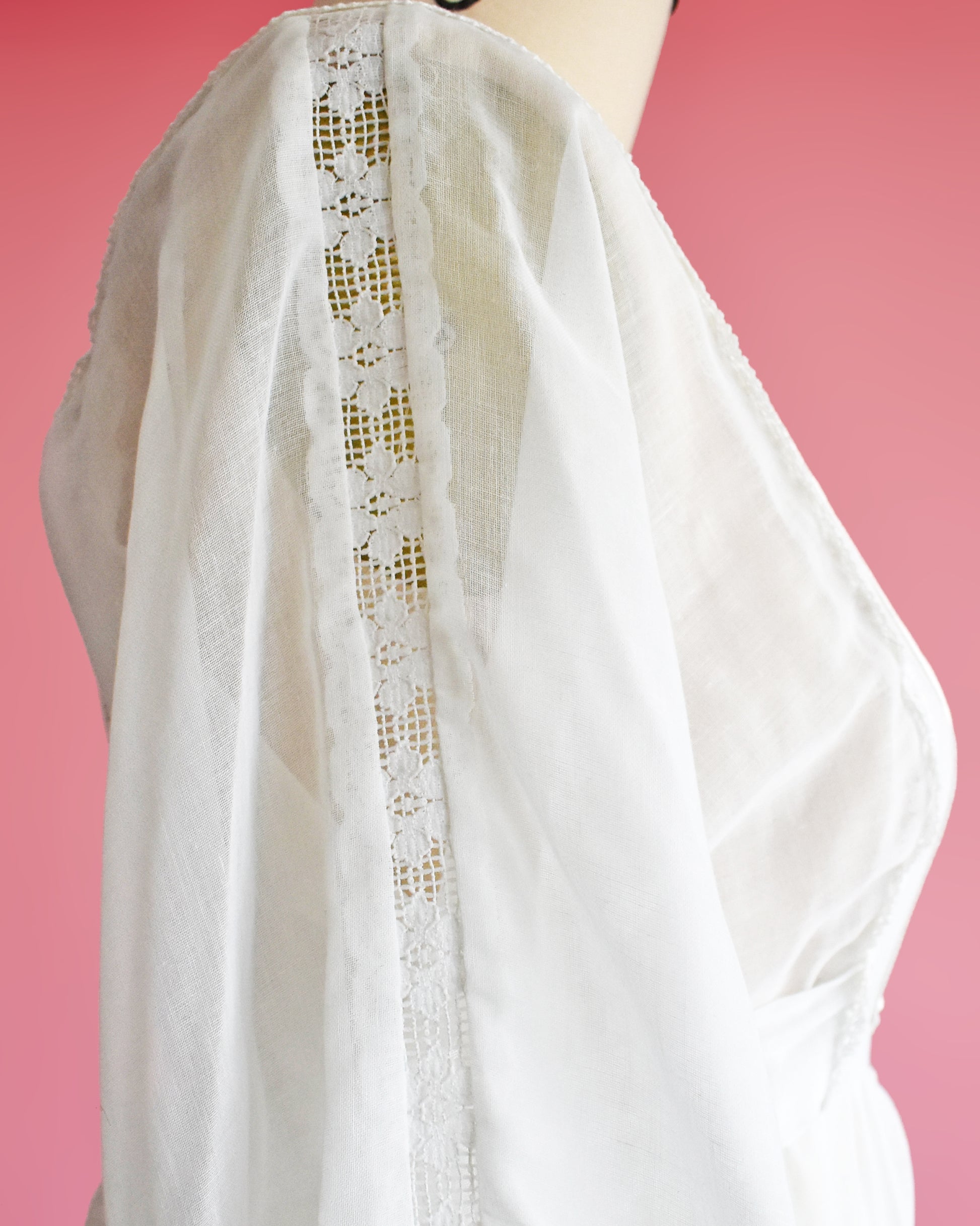 close up of the floral lace sleeve on a vintage 1970s white maxi dress on a mannequin against a pink background