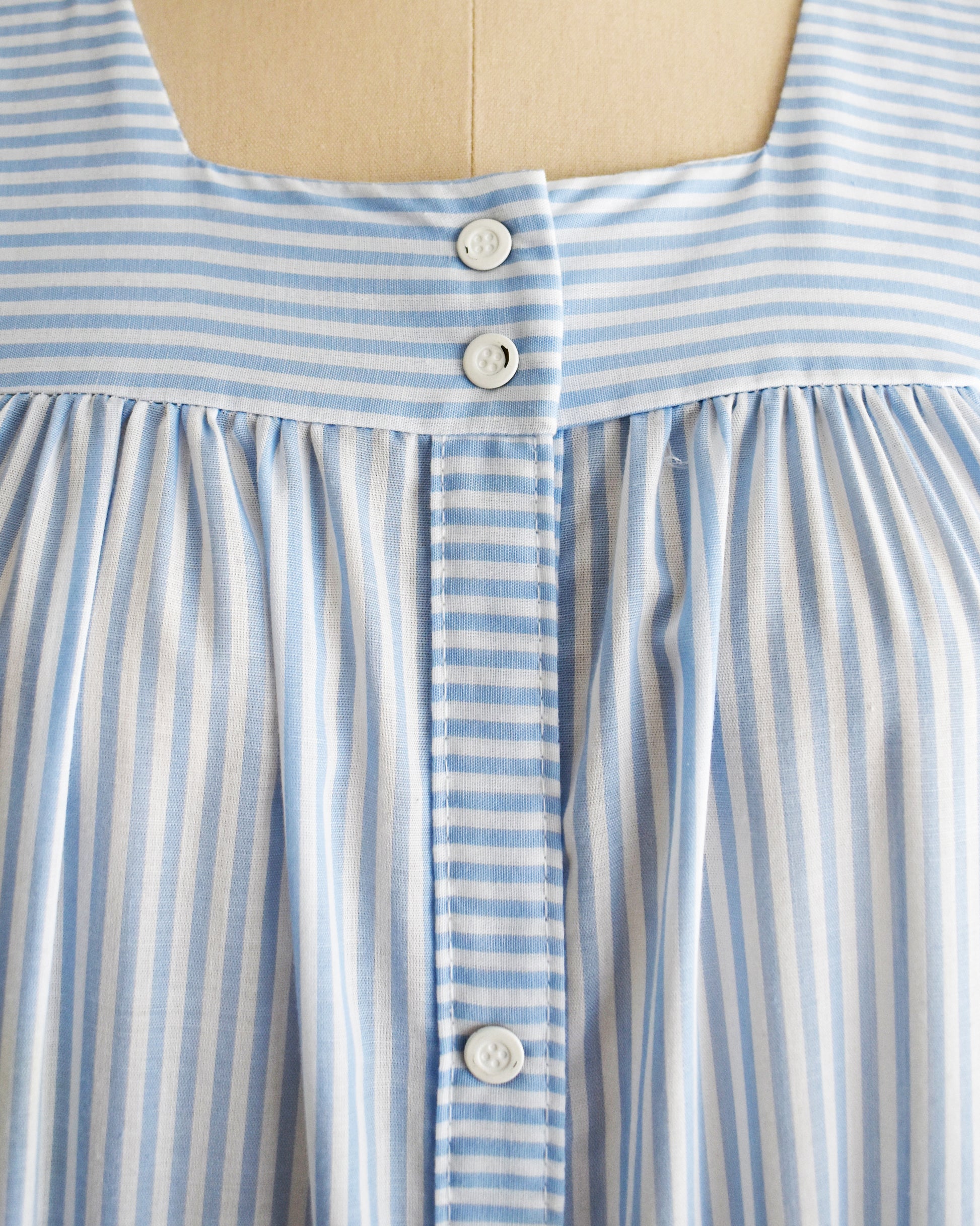 Close-up of a blue and white striped dress on a mannequin, which shows the white buttons that have a small amount of paint missing from them.