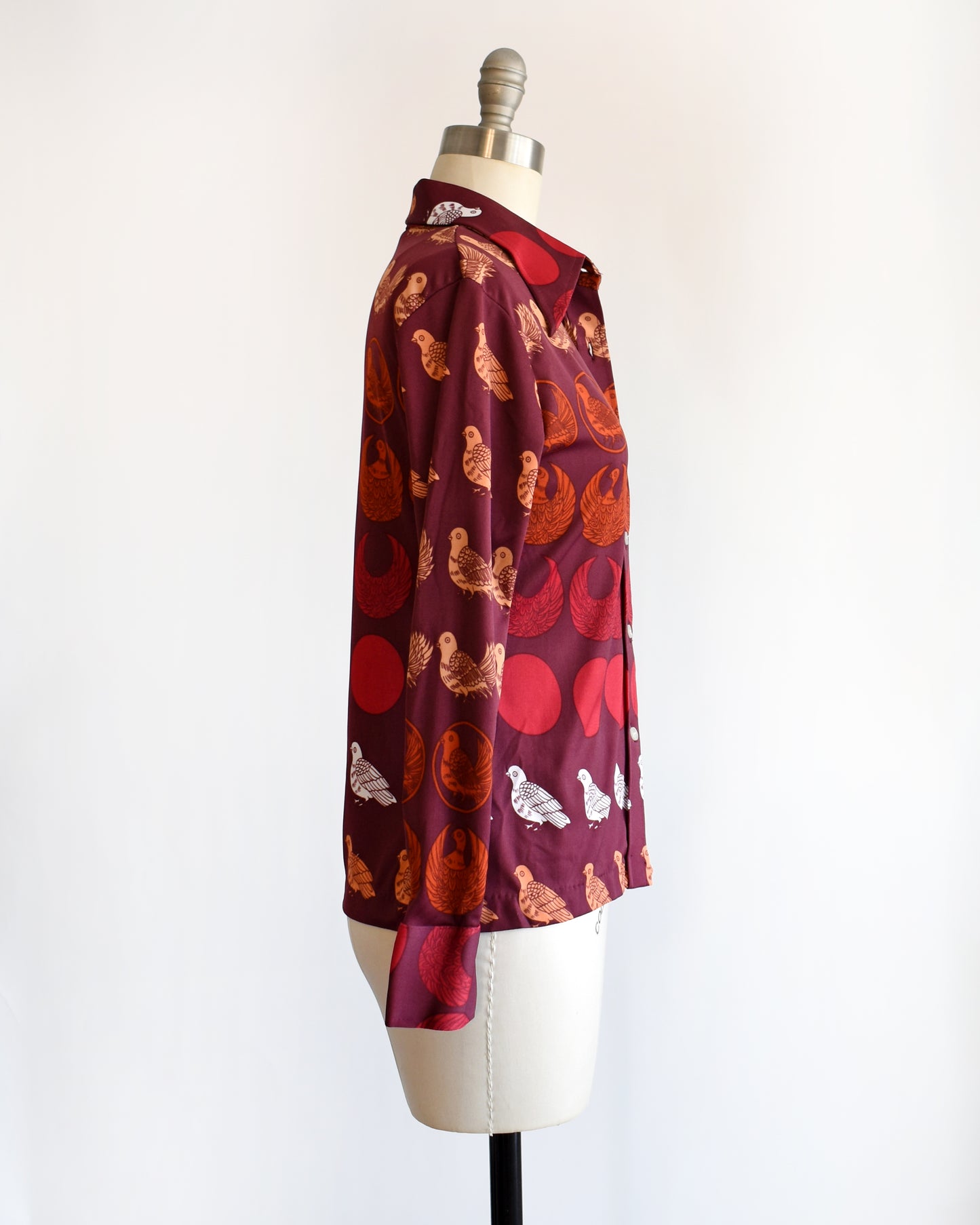 side view of a vintage 1970s red patterned bird shirt on a mannequin against a white background