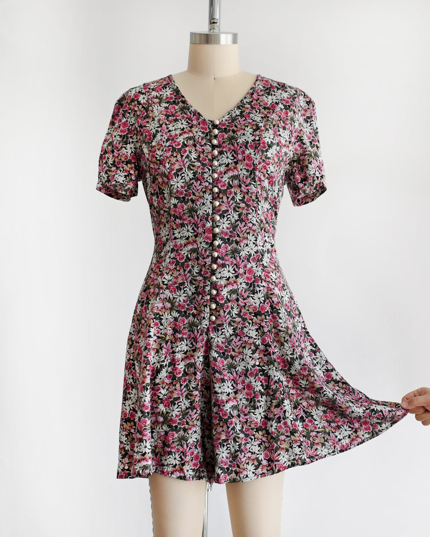 a vintage 1990s floral romper on a mannequin against a white background. a hand is pulling one of the shorts
