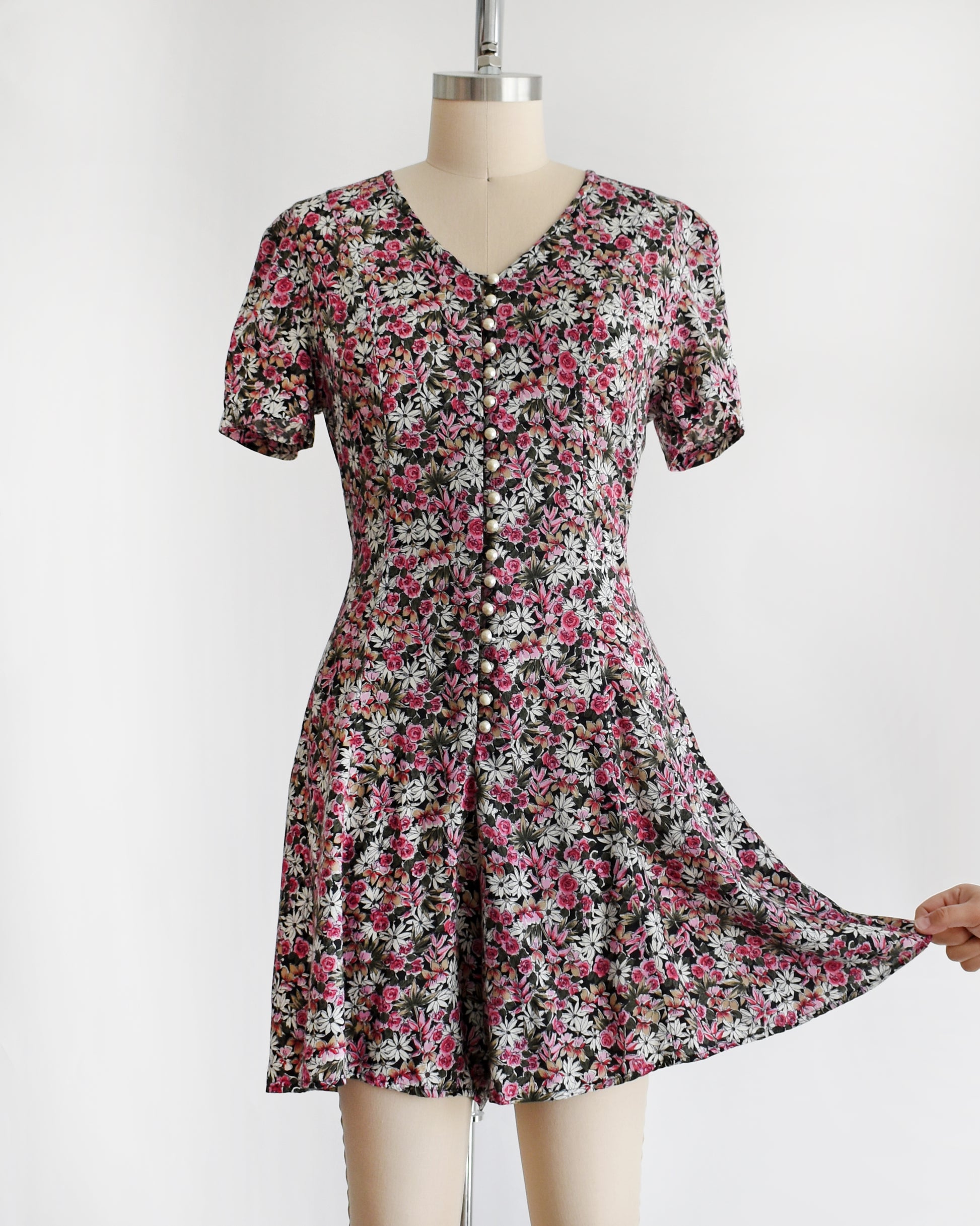 a vintage 1990s floral romper on a mannequin against a white background. a hand is pulling one of the shorts