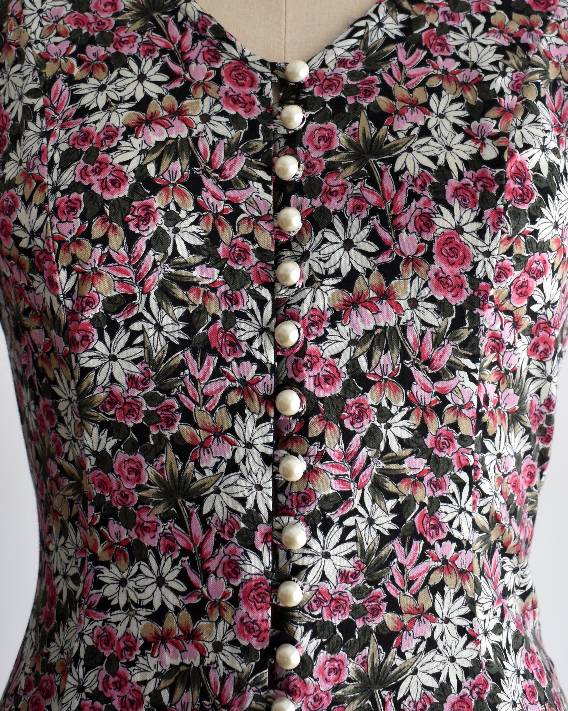 close up of the pearly buttons on a vintage 1990s floral romper on a mannequin against a white background