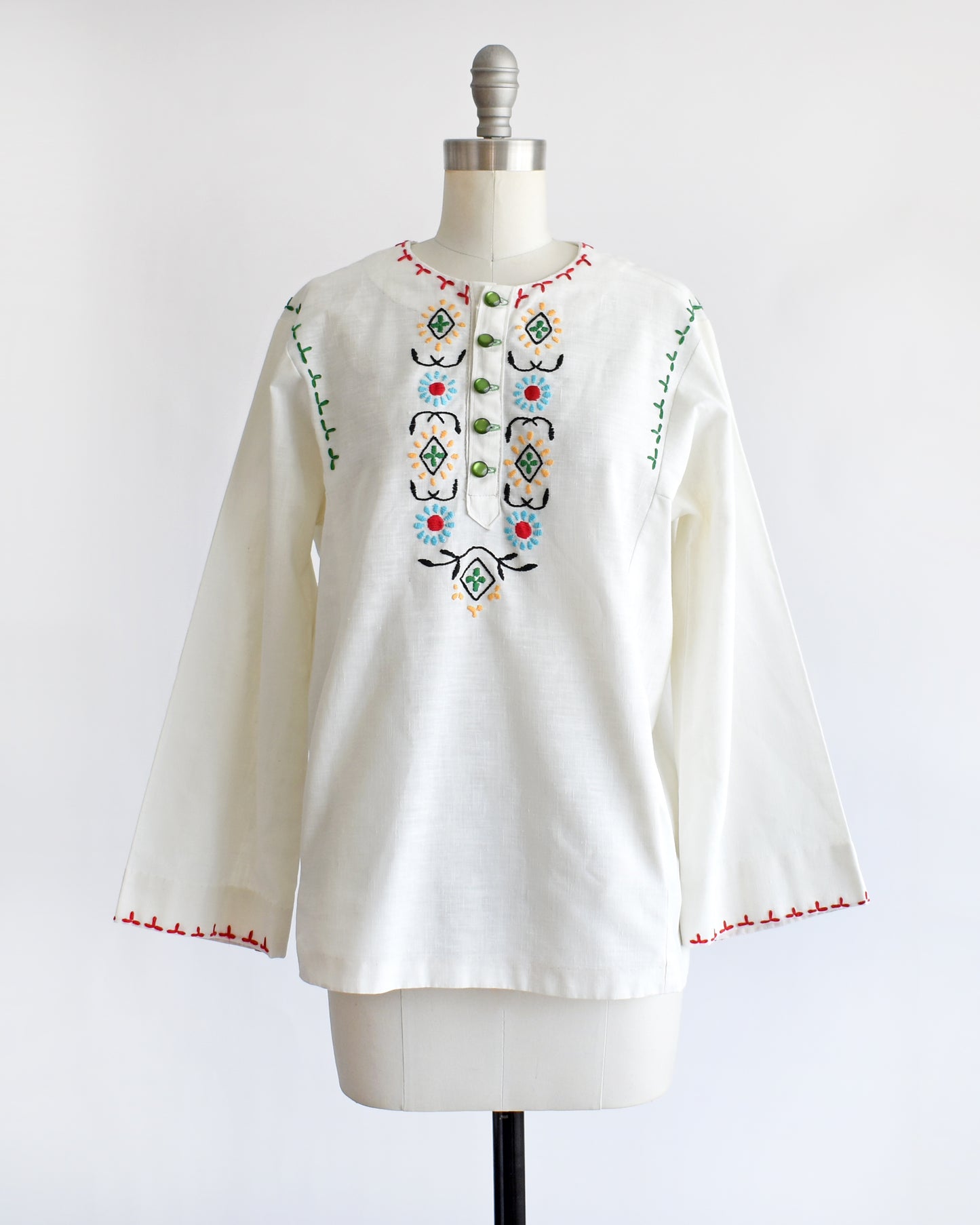 a vintage 1970s white blouse with colorful embroidery on a mannequin against a white background