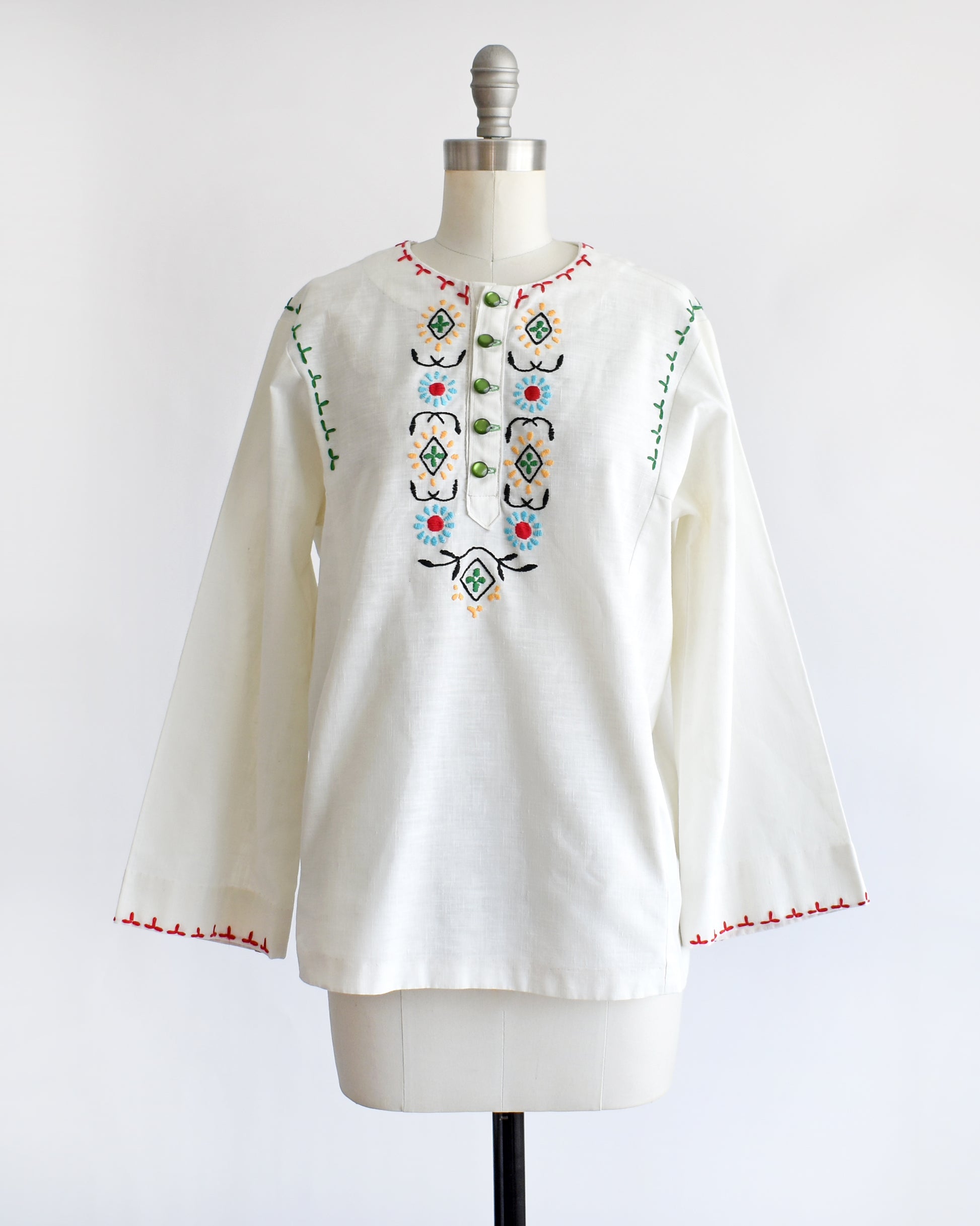 a vintage 1970s white blouse with colorful embroidery on a mannequin against a white background