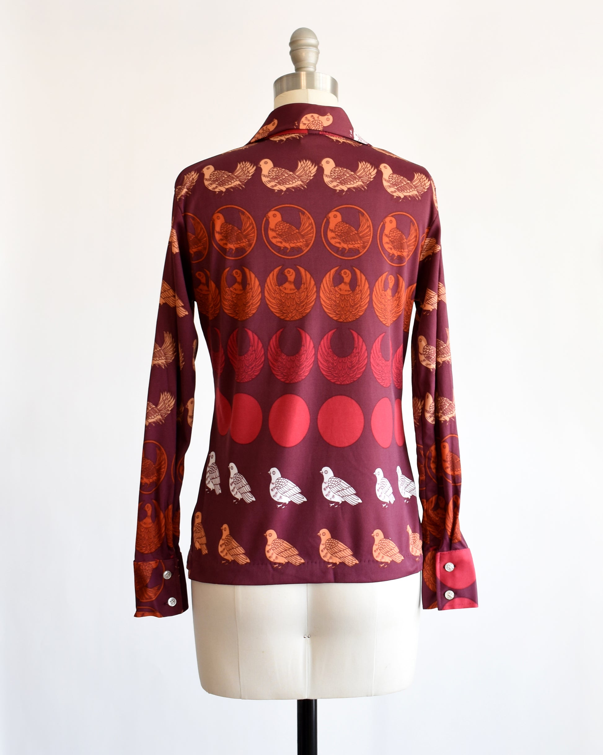 back view of a vintage 1970s red patterned bird shirt on a mannequin against a white background