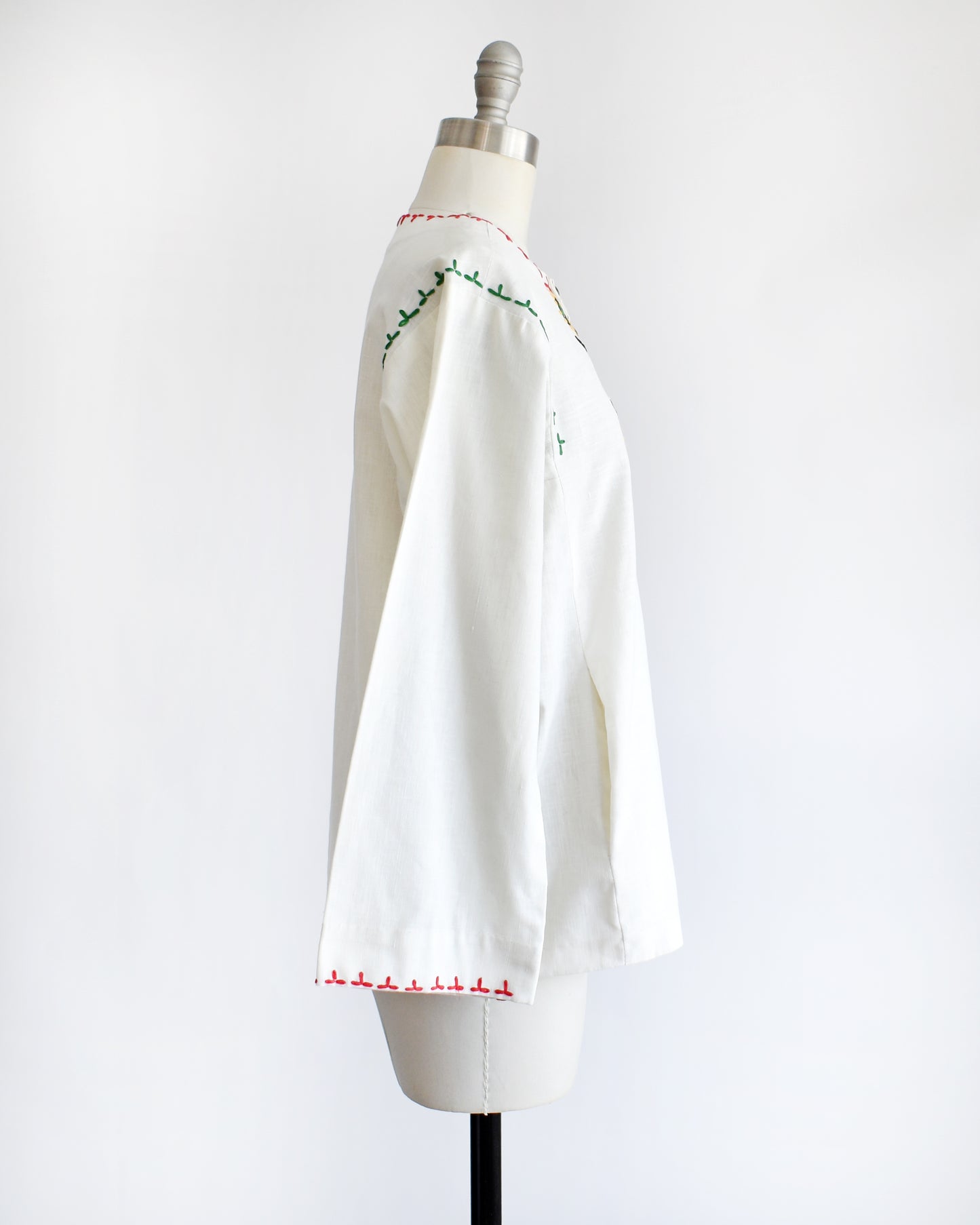 side view of a vintage 1970s white blouse with colorful embroidery on a mannequin against a white background