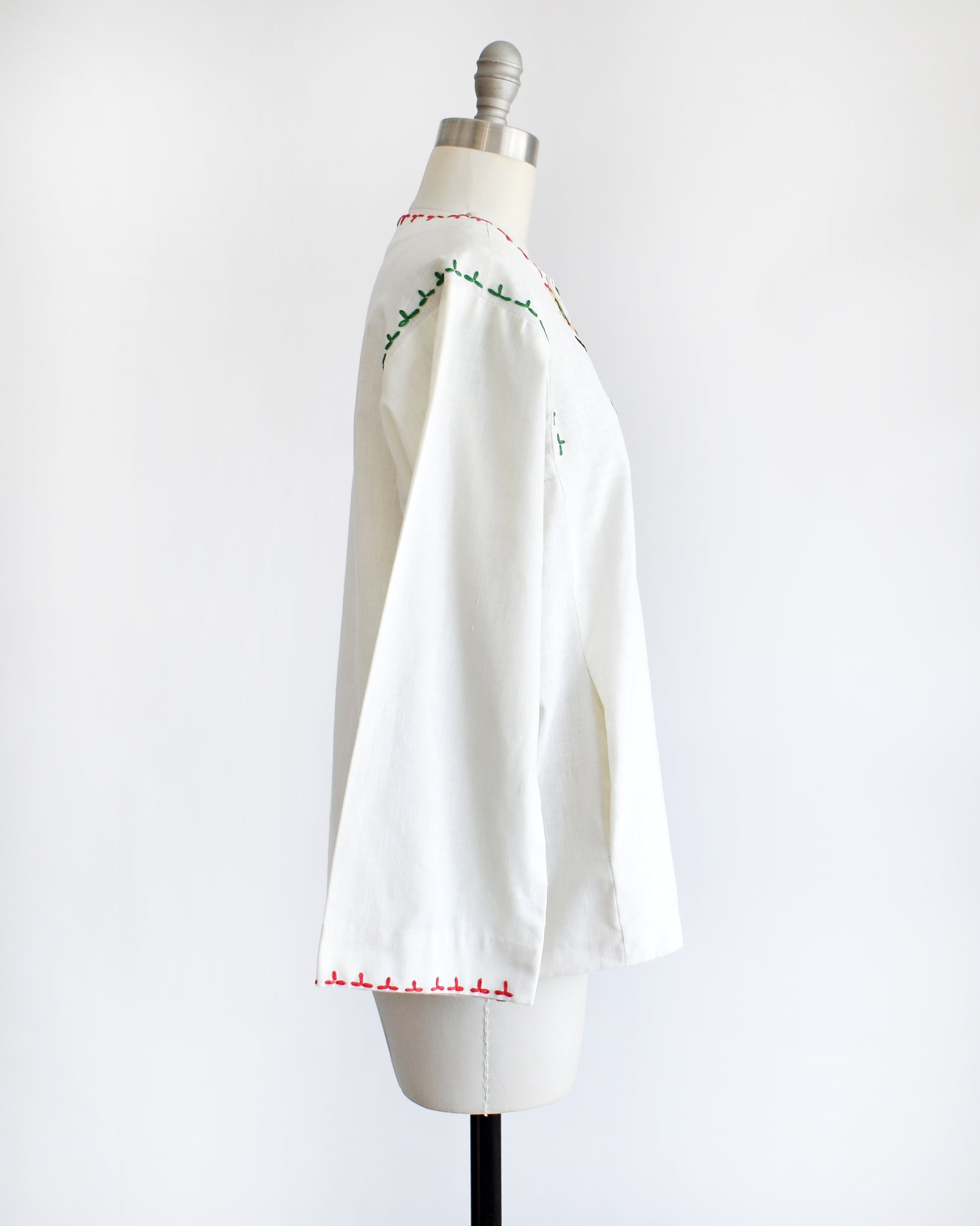 side view of a vintage 1970s white blouse with colorful embroidery on a mannequin against a white background