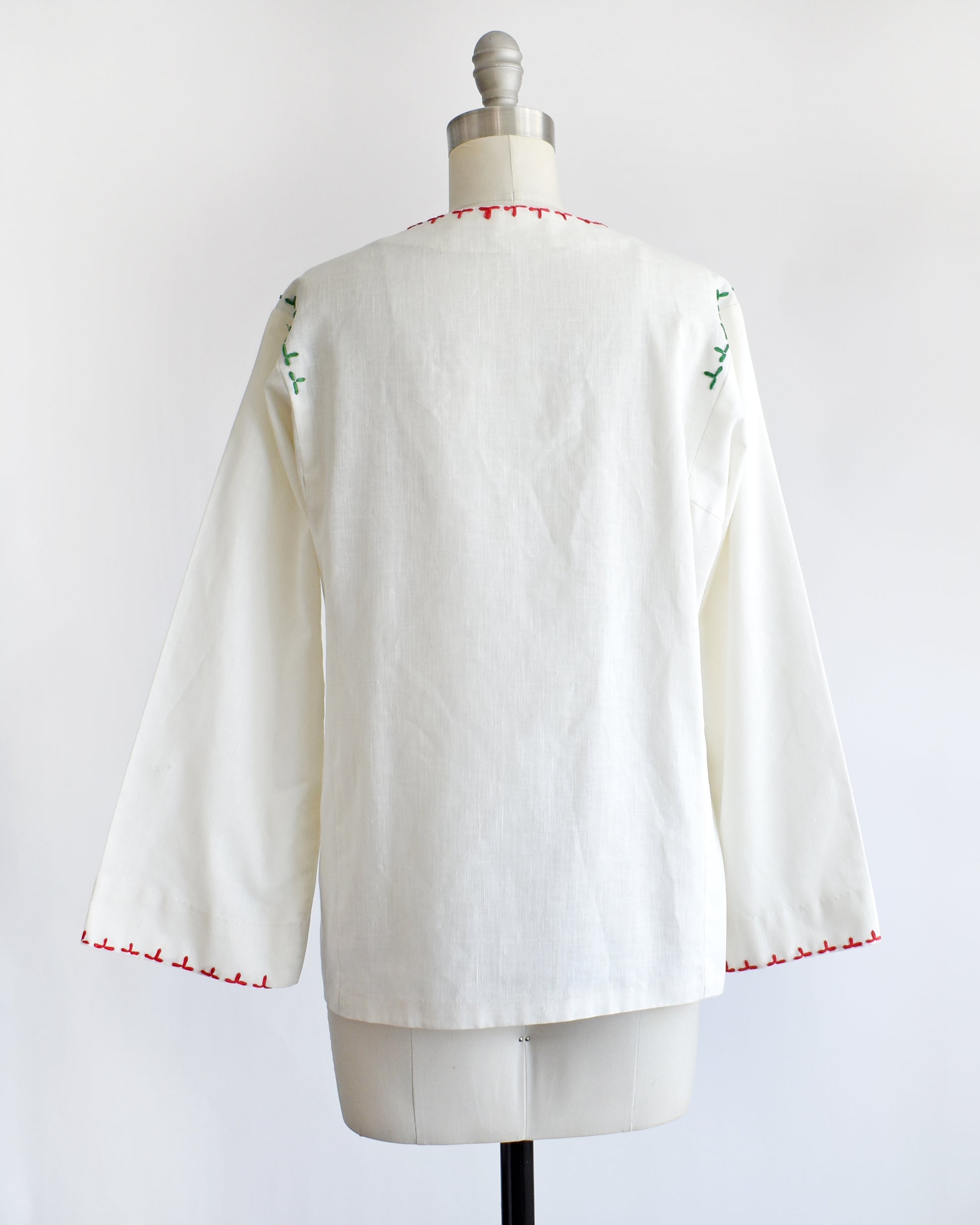 back view of a vintage 1970s white blouse with colorful embroidery on a mannequin against a white background