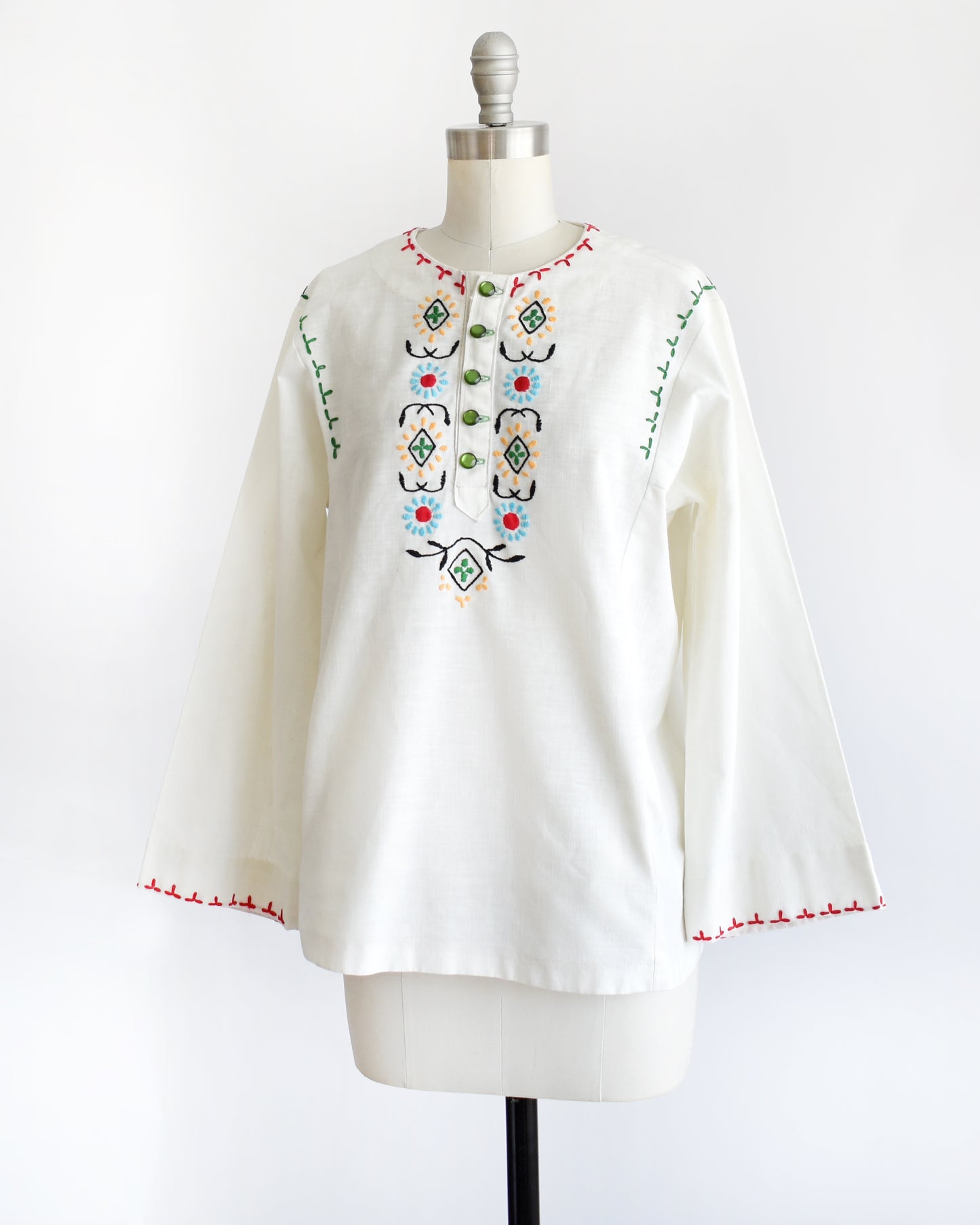 side front view of a vintage 1970s white blouse with colorful embroidery on a mannequin against a white background