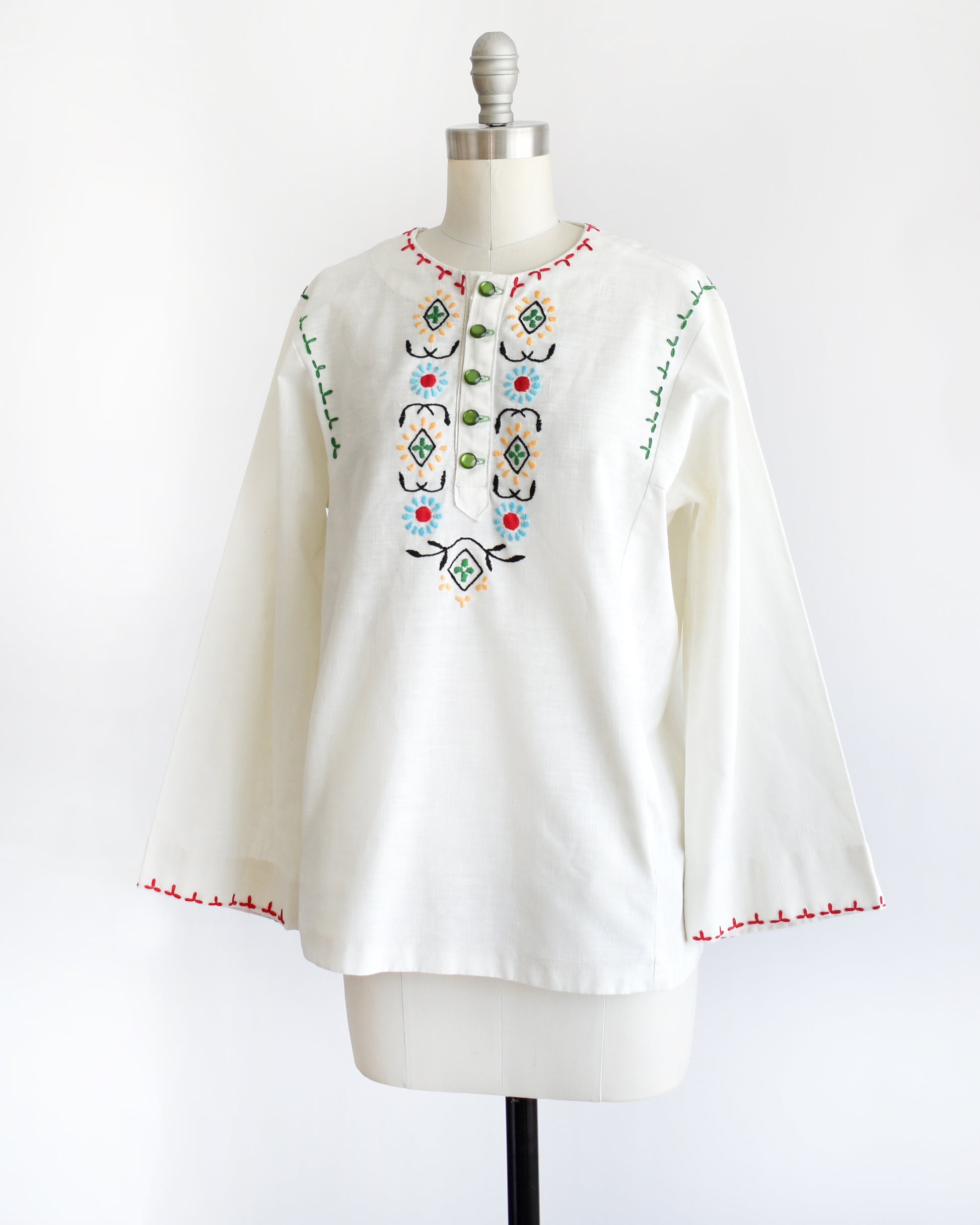side front view of a vintage 1970s white blouse with colorful embroidery on a mannequin against a white background