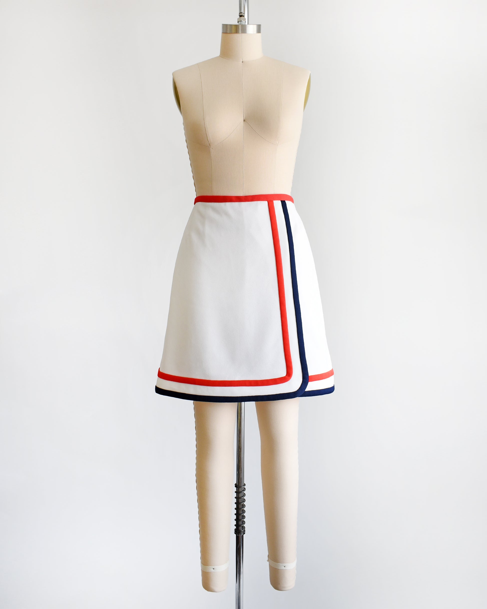 A vintage 1970s white skort with red and navy trim on a dress form against a white background