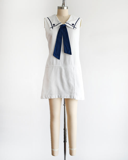 a vintage 1960s white romper dress with a navy blue bow on a mannequin against a white background