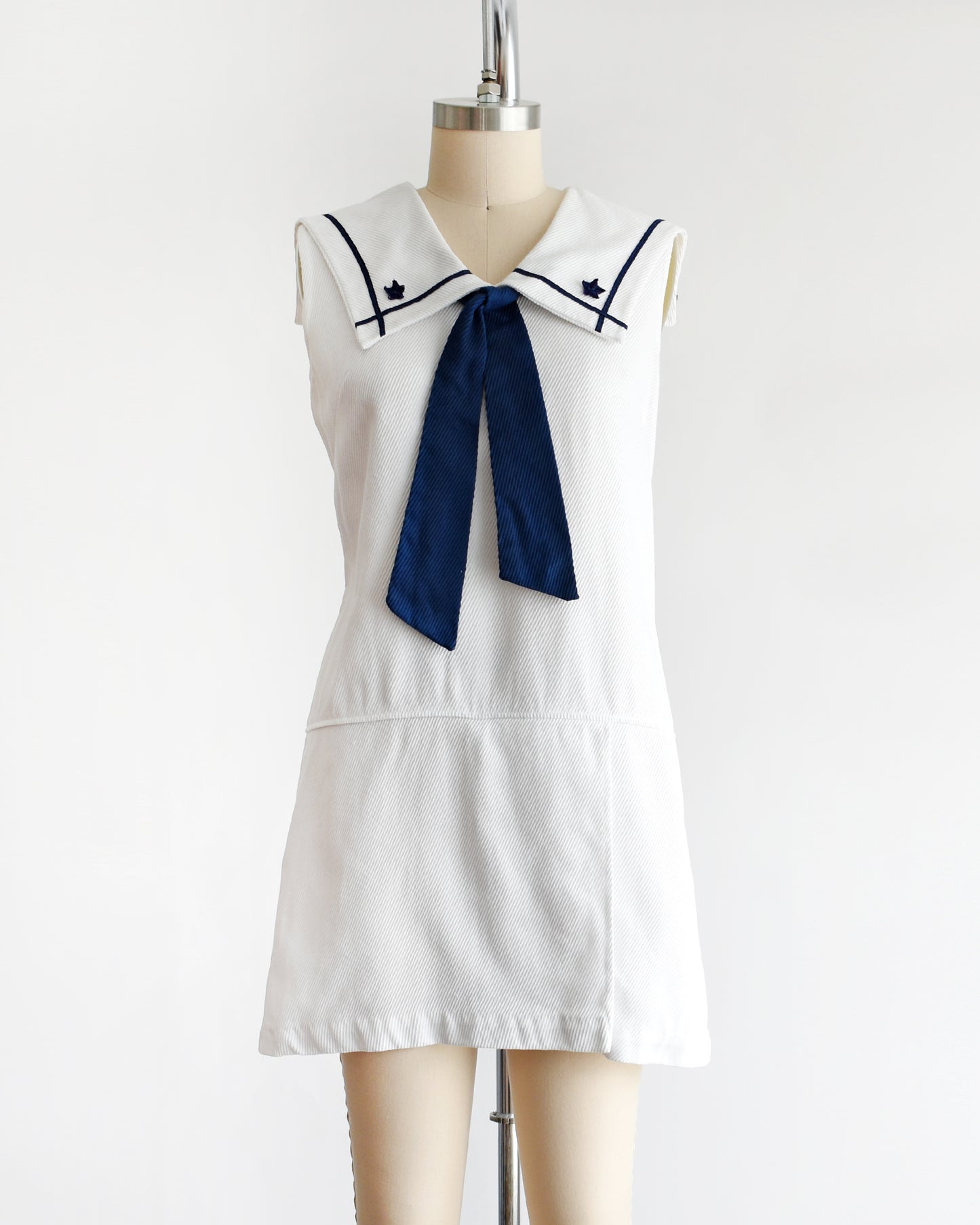 a vintage 1960s white romper dress with a navy blue bow on a mannequin against a white background