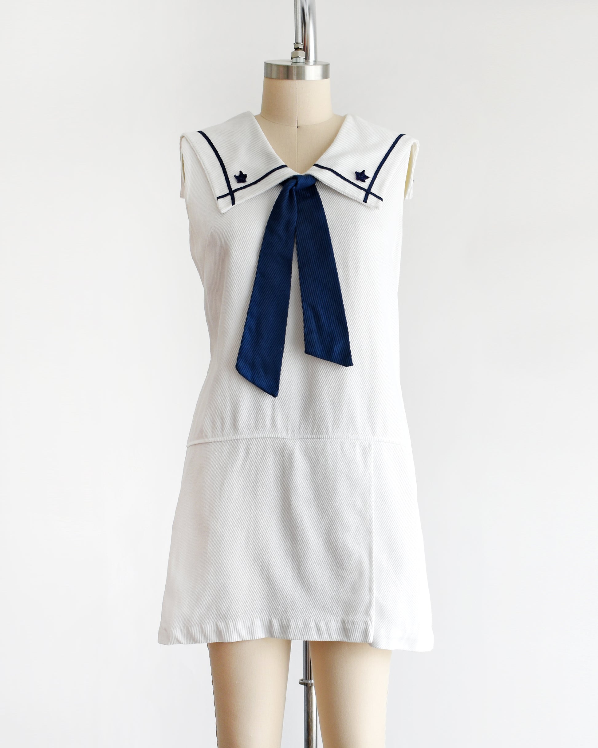 a vintage 1960s white romper dress with a navy blue bow on a mannequin against a white background