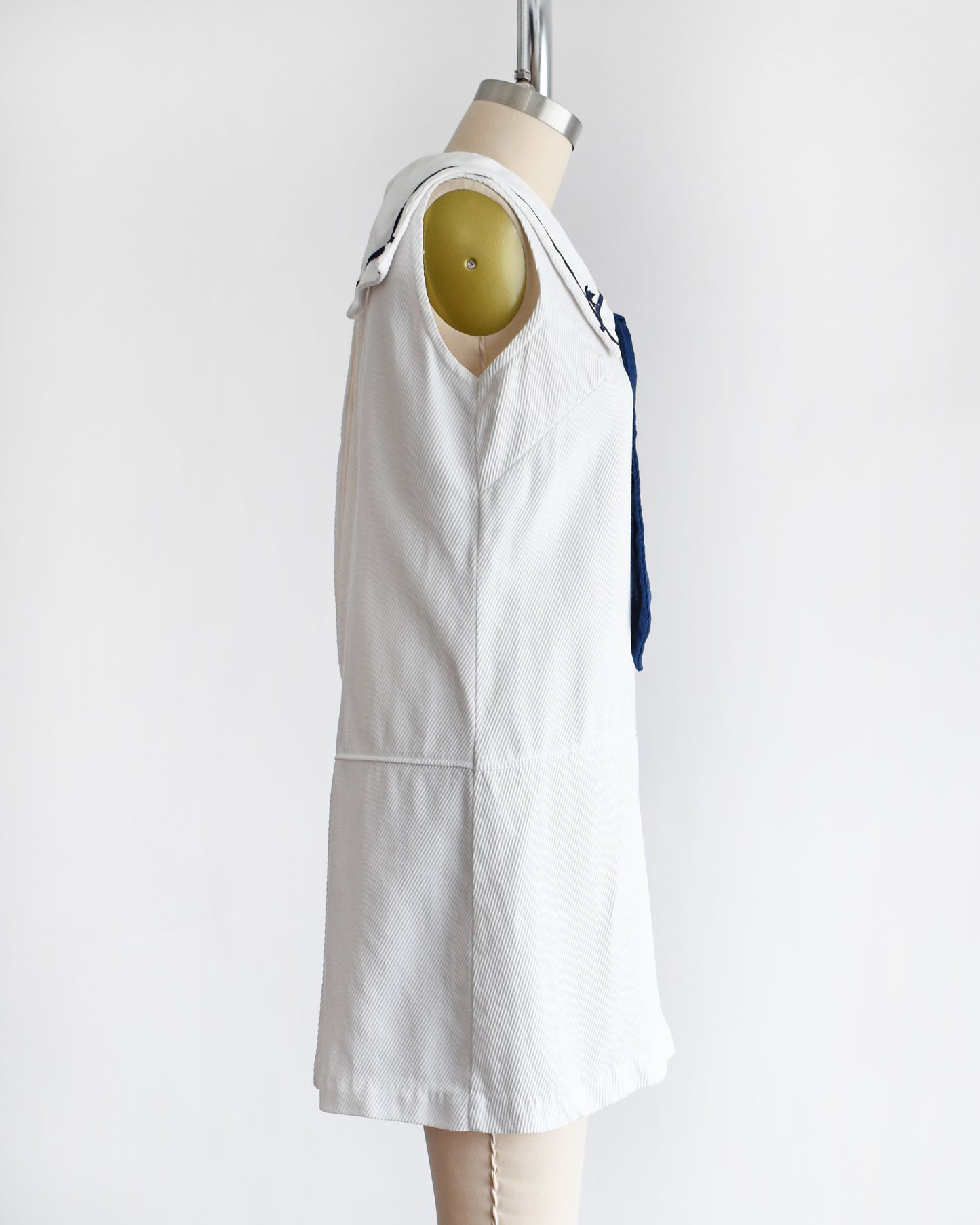 side view of a vintage 1960s white romper dress with a navy blue bow on a mannequin against a white background
