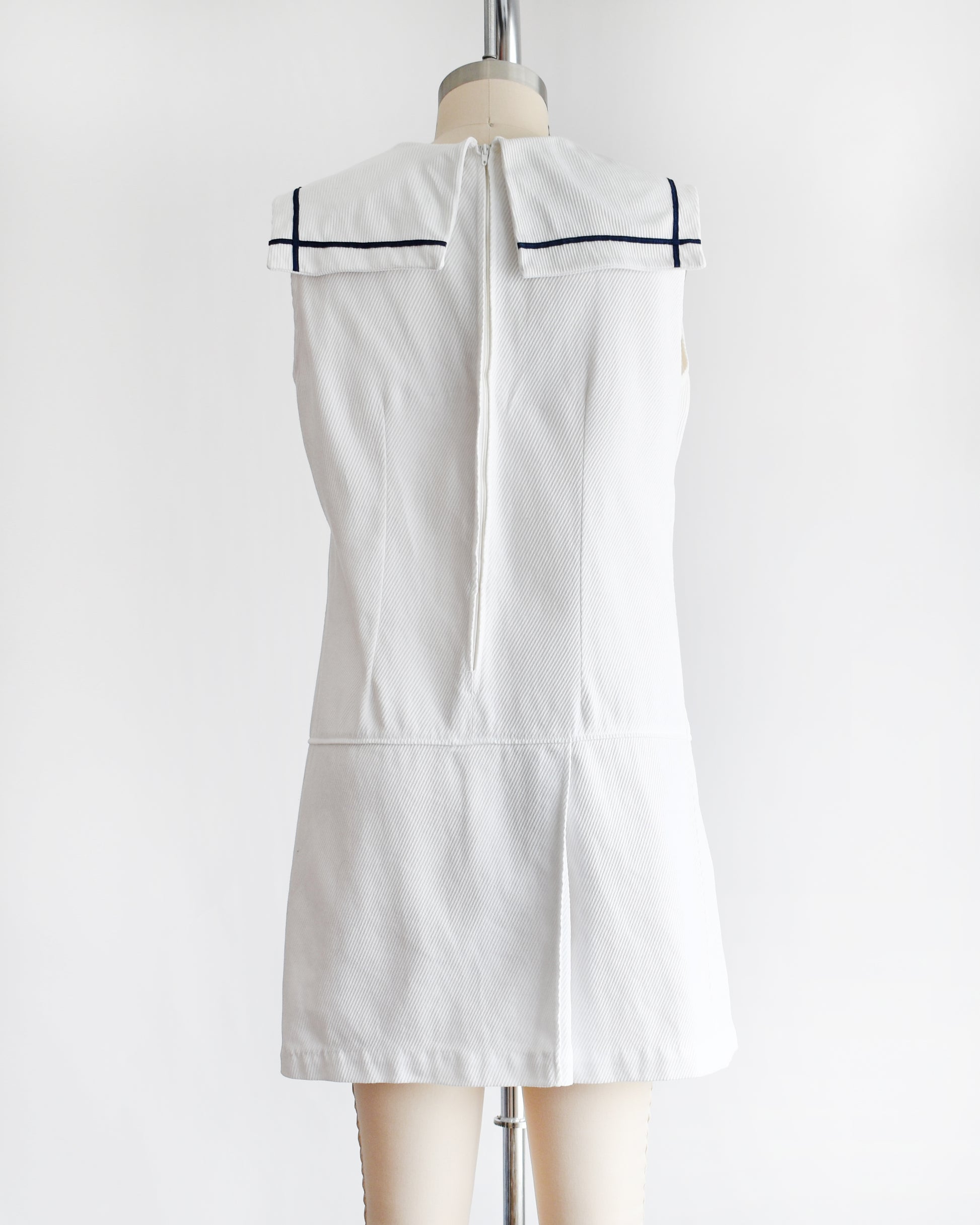 back view of a vintage 1960s white romper dress with a navy blue bow on a mannequin against a white background