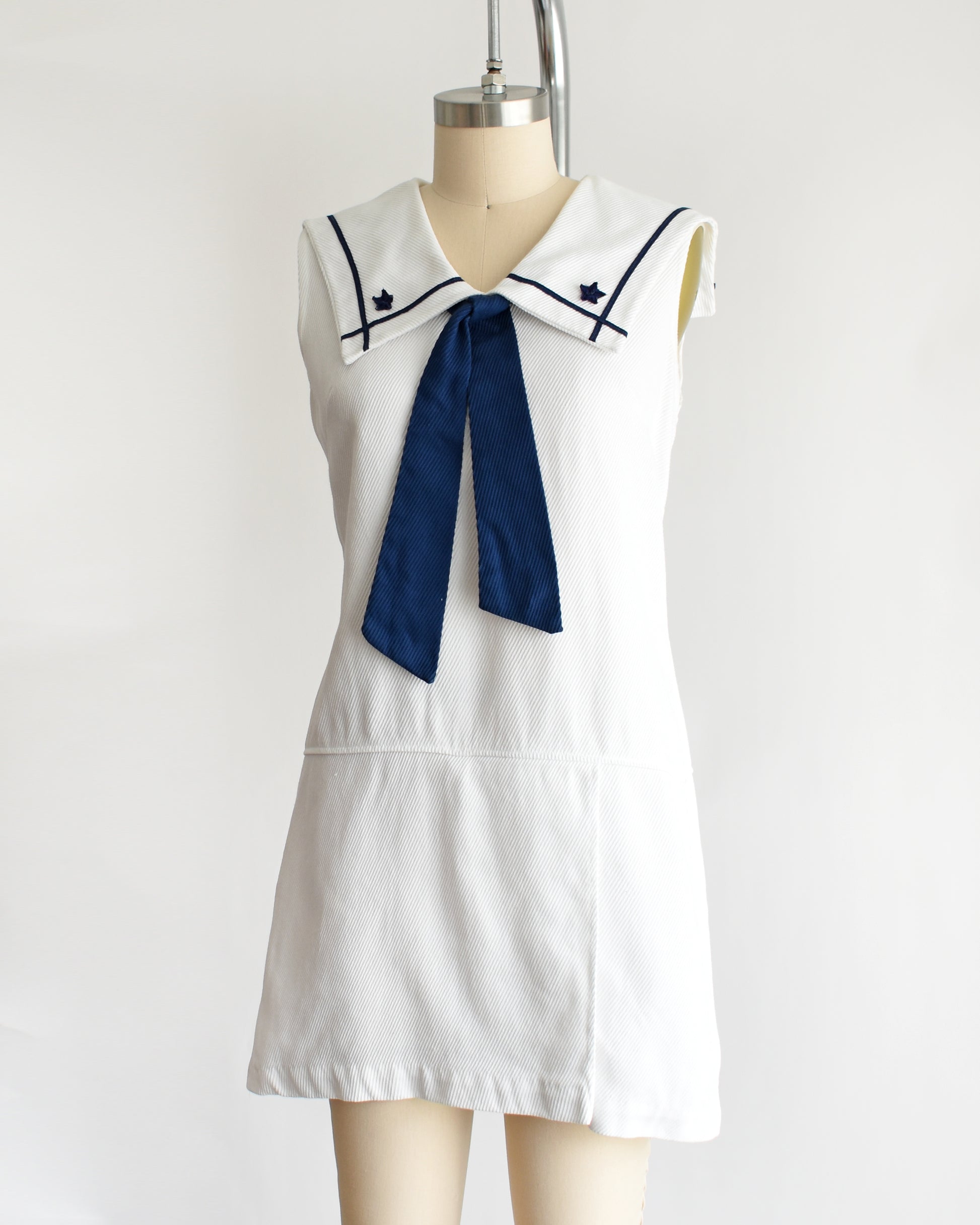 side front view of a vintage 1960s white romper dress with a navy blue bow on a mannequin against a white background