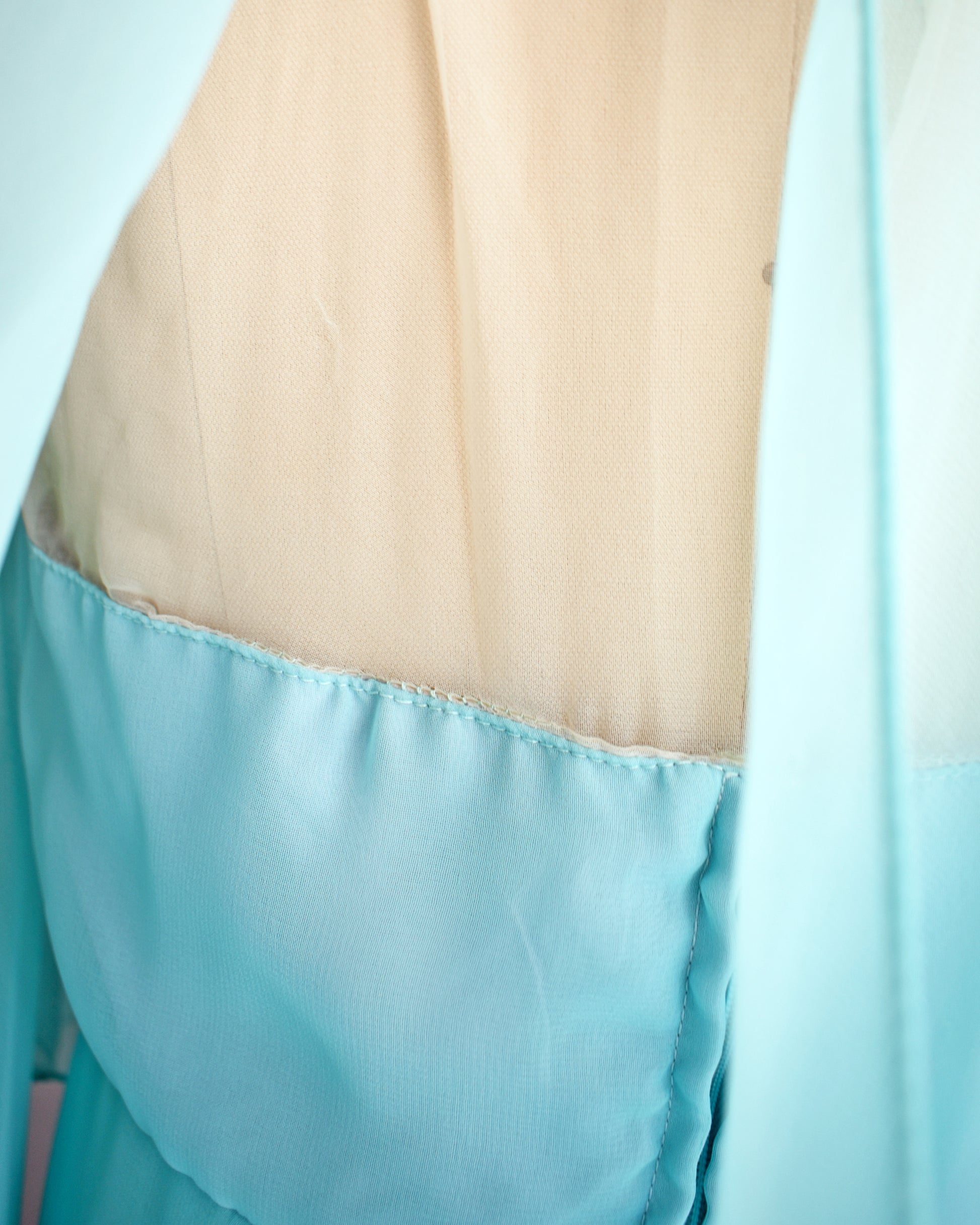 close up of the beige lining on the bodice of a vintage 1960s light blue ruffled maxi dress on a mannequin against a white background