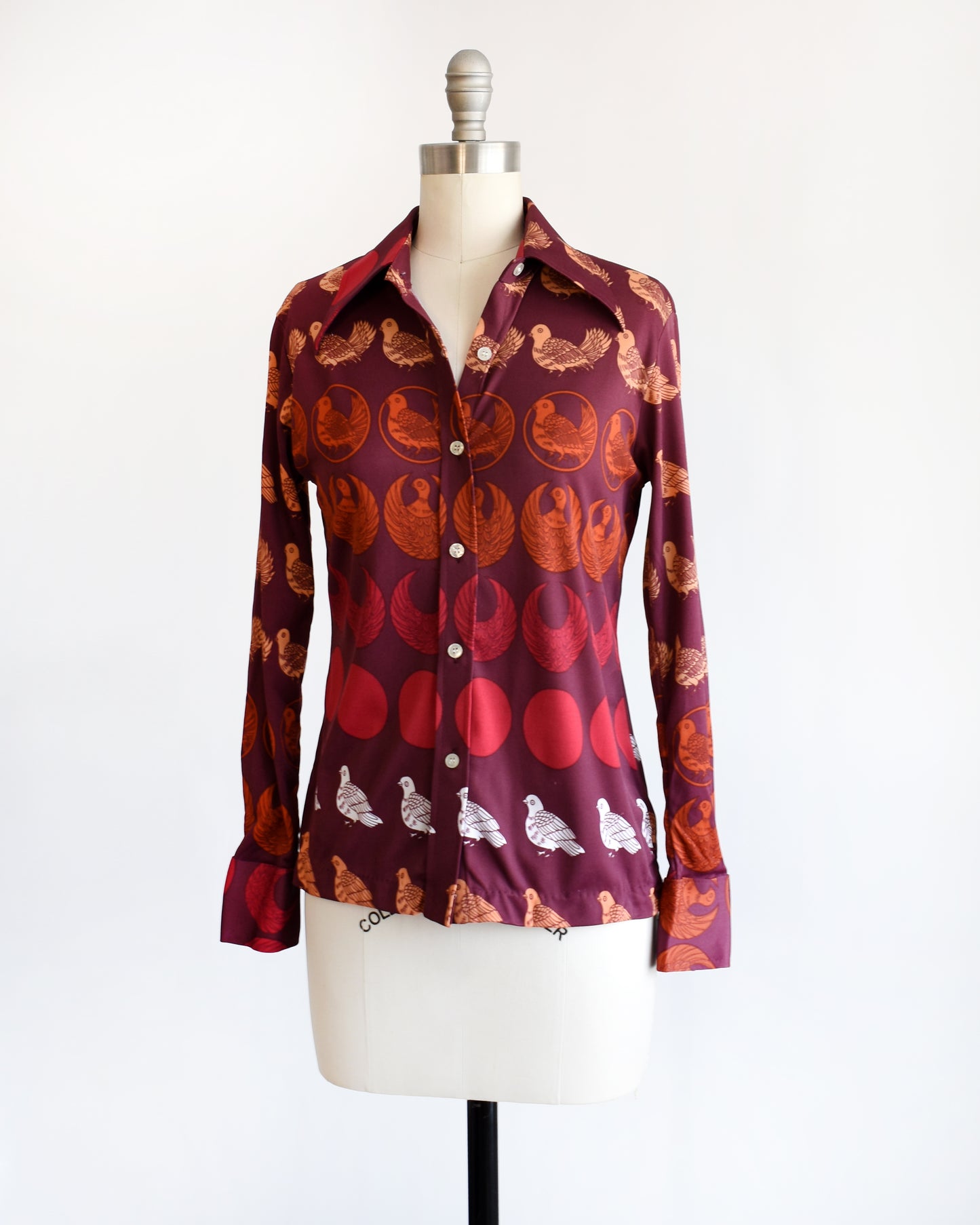 side front view of a vintage 1970s red patterned bird shirt on a mannequin against a white background. the top two buttons are unbuttoned in this photo